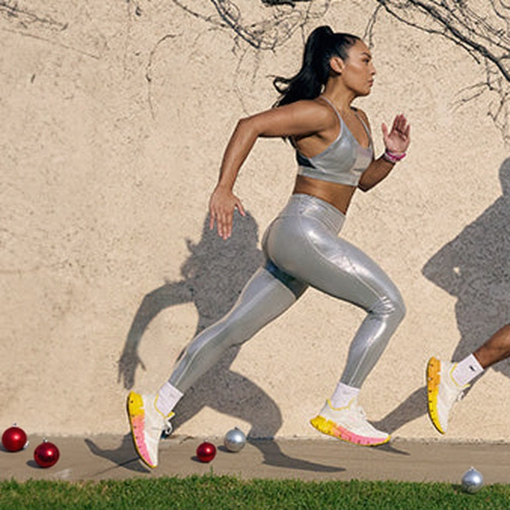 Woman in metallic silver athletic wear running outdoors with colorful shoes.