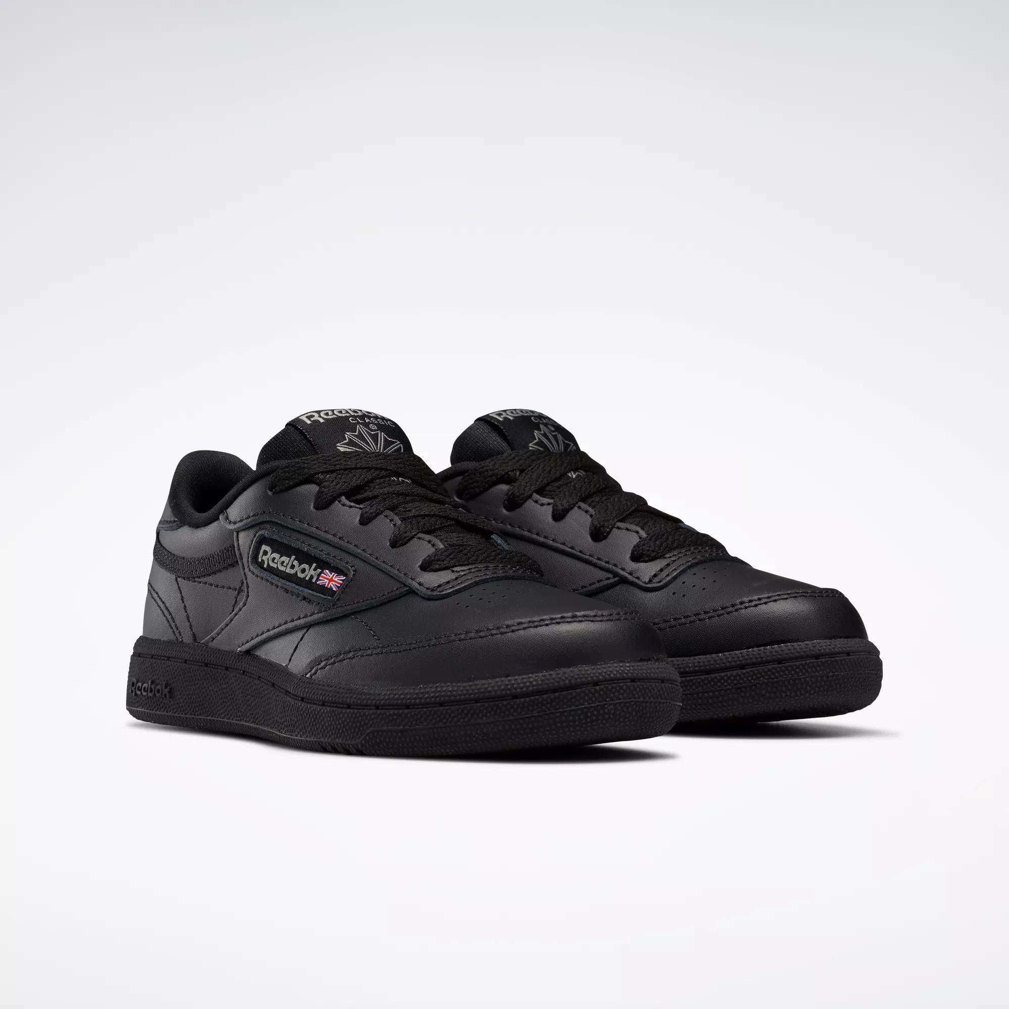 A pair of black Reebok Kids' Club C Shoes for little kids with laces, leather upper, Reebok branding, and Union Jack flag on the side are displayed on a light background.