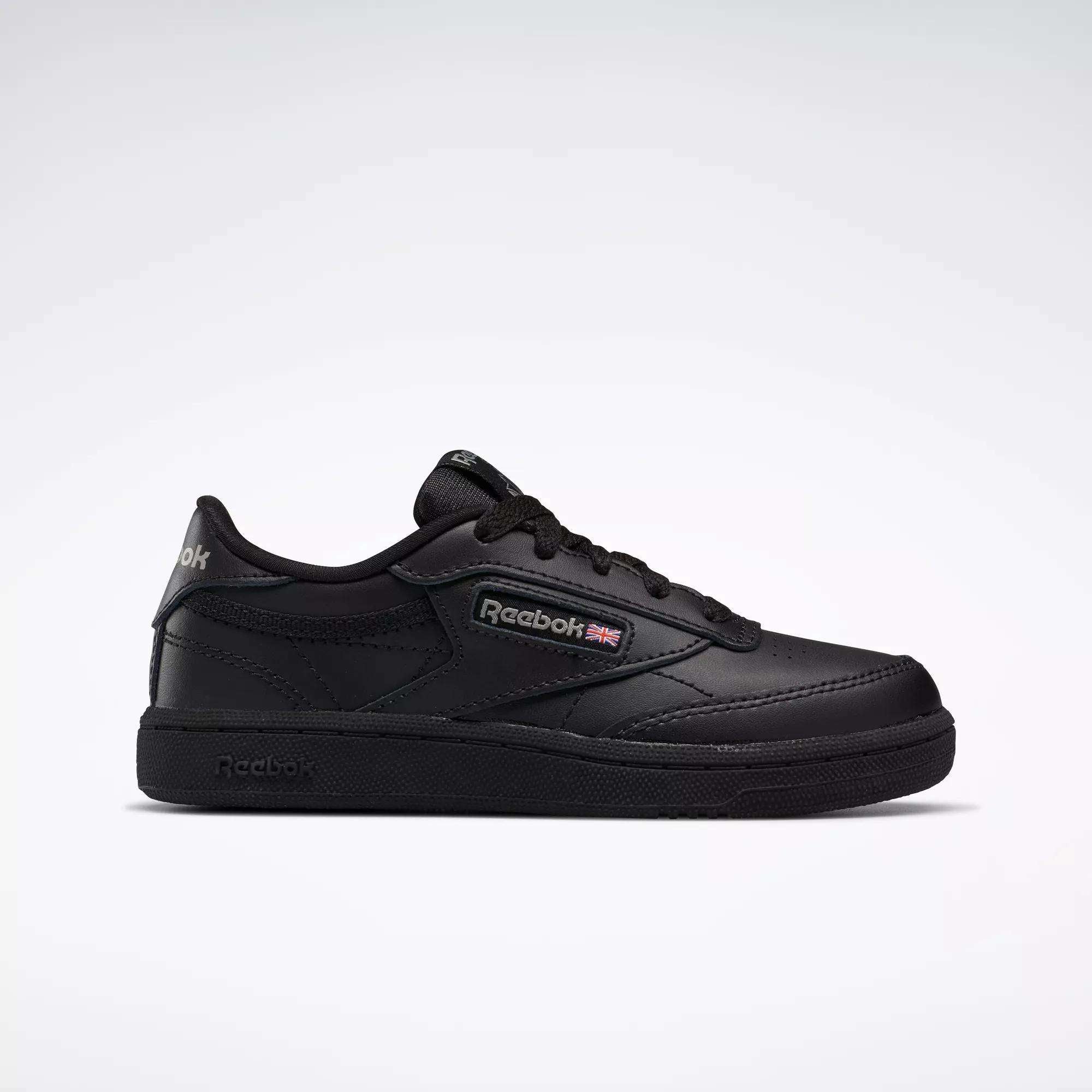 The Kids' Club C Shoes - Little Kids by Reebok are black low-top sneakers with a leather upper, Reebok logo and British flag on the side, black laces, and a black rubber sole, shown against a plain light gray background.
