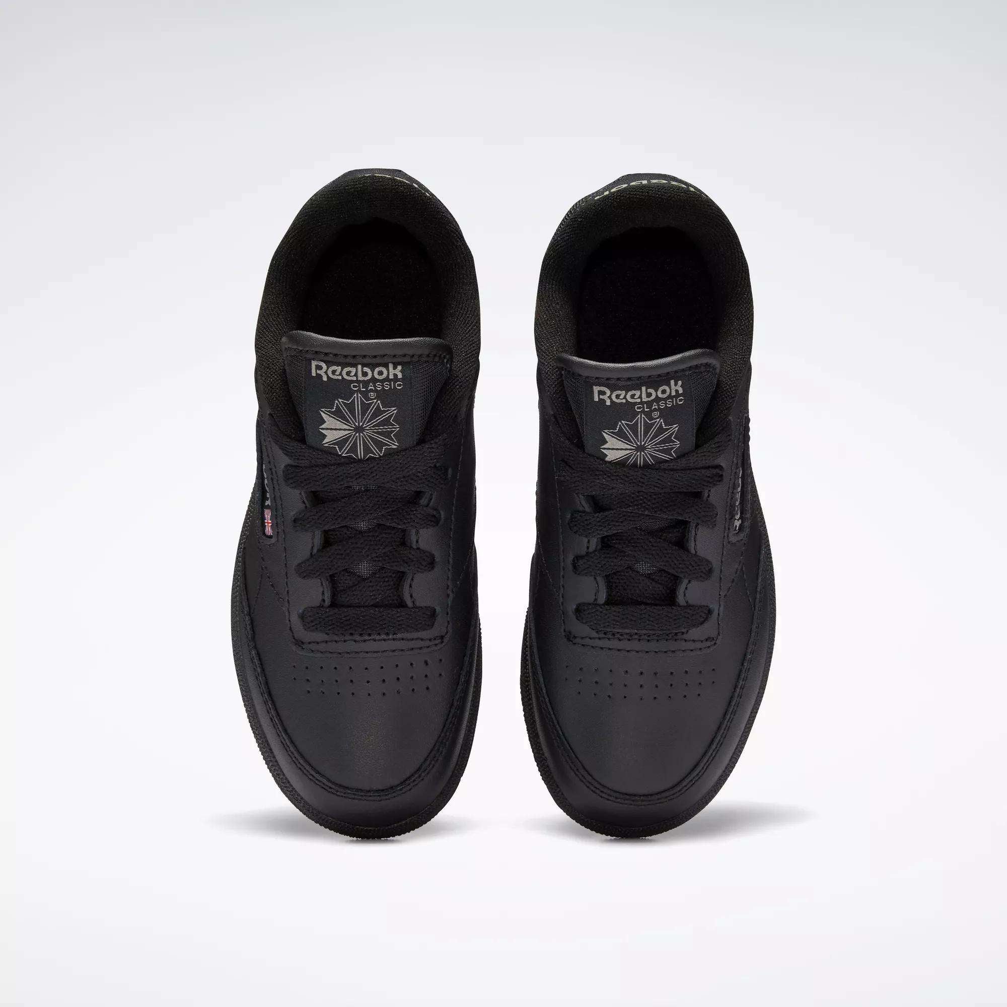 Top view of Kids' Club C Shoes by Reebok: classic black sneakers featuring a durable leather upper, black laces, perforated toe details, and Reebok logos on each tongue.
