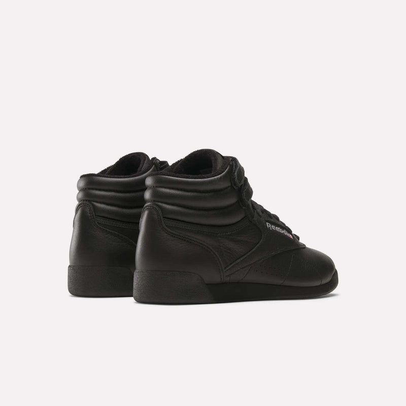 A pair of Women's Freestyle Hi Shoes by Reebok are shown from the back and side on a white background. These black leather high tops feature padded collars and subtle branding, ideal for women’s fitness enthusiasts.