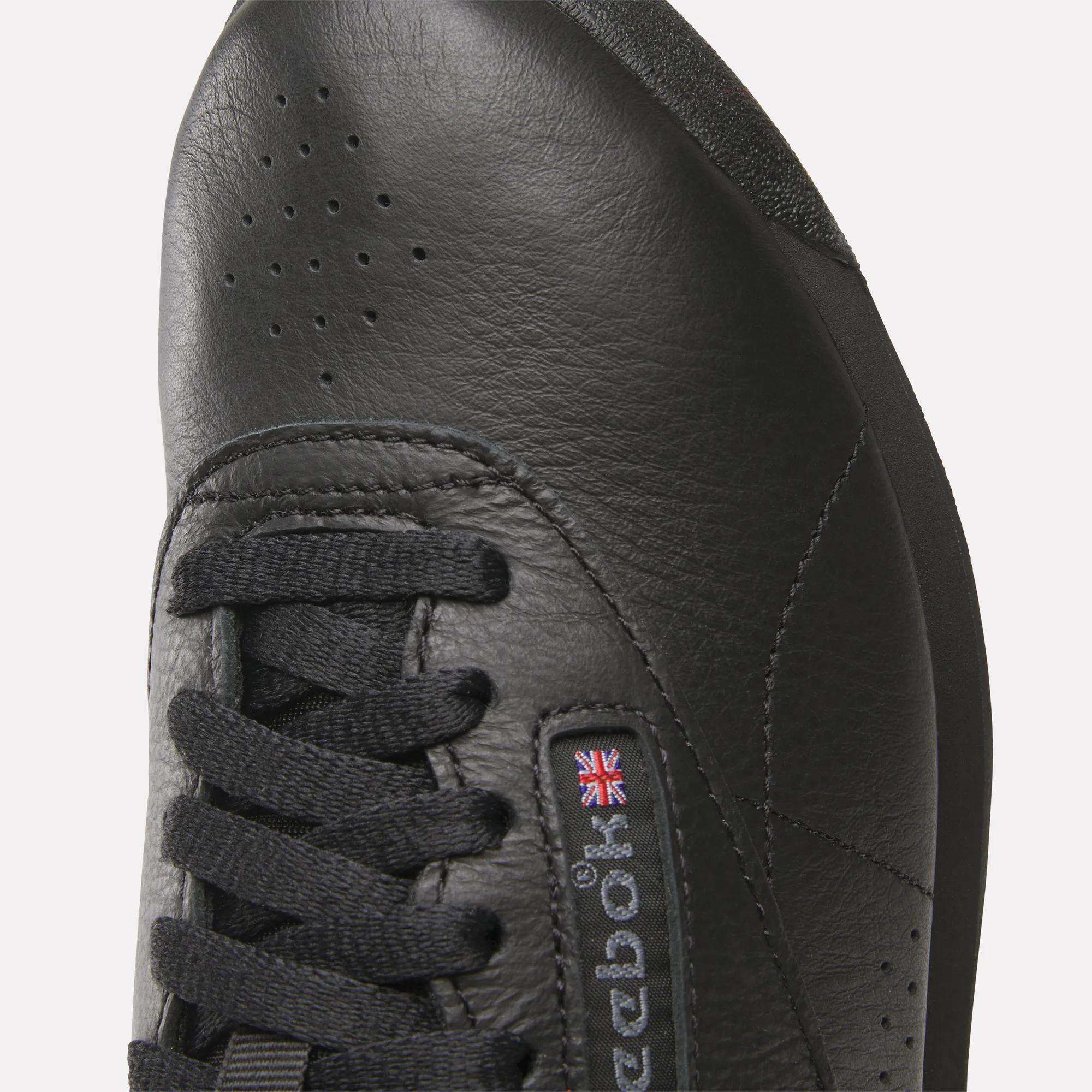 Close-up of the toe and laces on Reebok Women's Freestyle Hi Shoes, with black stitching, perforated details, and a small embroidered UK flag near the logo—ideal for women's fitness or adding classic style to your high top look.