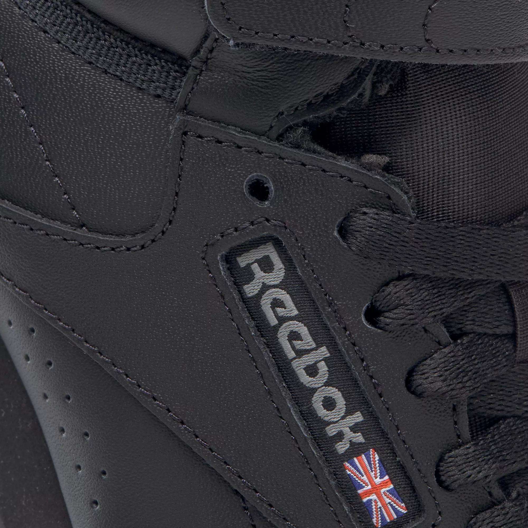 Close-up of the Reebok Women's Freestyle Hi Shoes, a black high-top sneaker with black laces, detailed stitching, and the Reebok logo plus Union Jack flag on the side—ideal for women’s fitness enthusiasts.