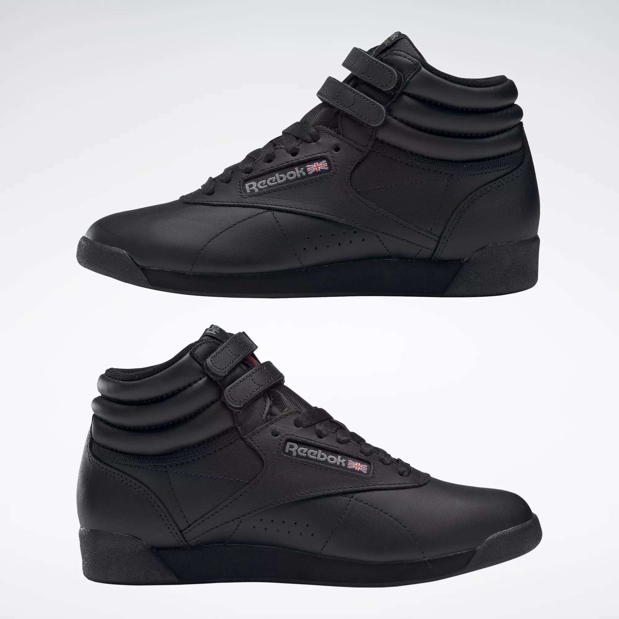 Two black Reebok Women's Freestyle Hi Shoes are displayed side by side against a light background, featuring velcro straps and the Reebok logo with a UK flag—ideal for women's fitness routines.