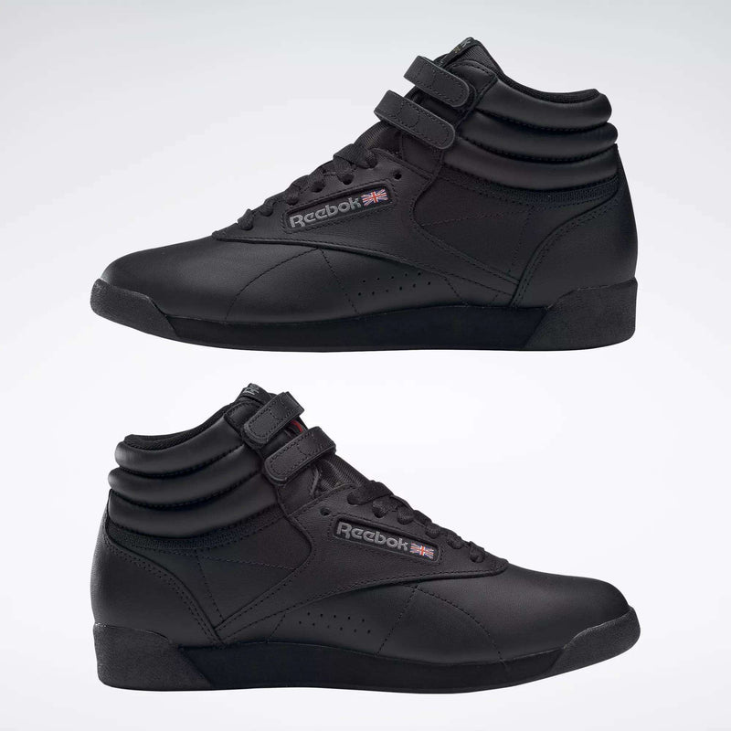 Two black Reebok Women's Freestyle Hi Shoes are displayed side by side against a light background, featuring velcro straps and the Reebok logo with a UK flag—ideal for women's fitness routines.