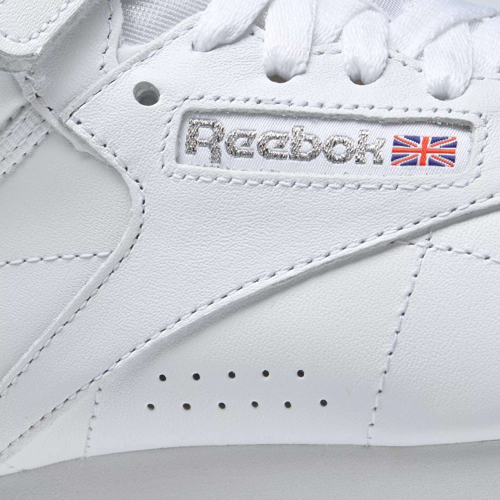 Close-up of the Women's Freestyle Hi Shoes by Reebok, showcasing the stitched logo, Union Jack flag, and crisp white laces—ideal for women who value both style and comfort in their fitness footwear.