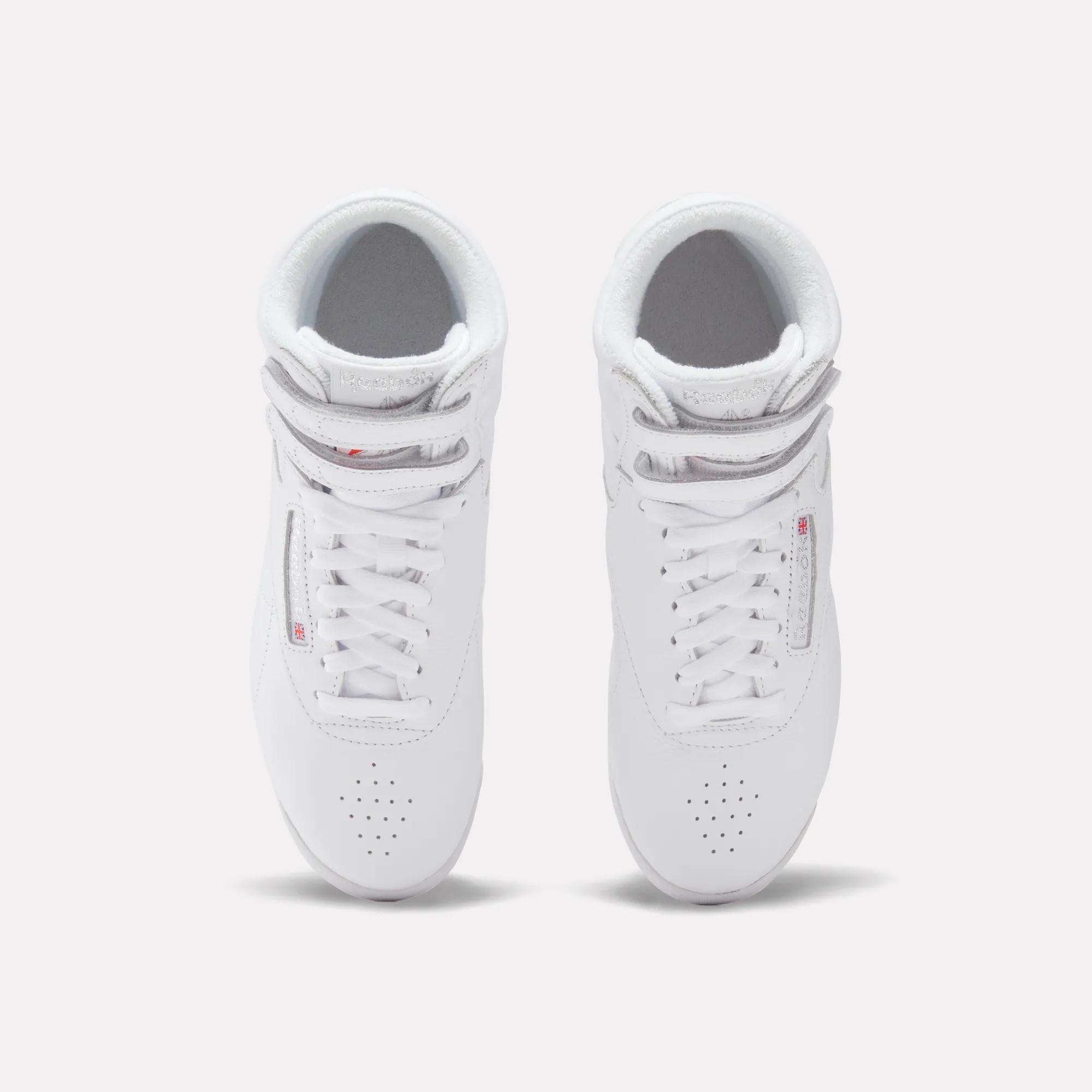 Top view of Women's Freestyle Hi Shoes by Reebok, white high tops with laces, displayed side by side on a light background—stylish sneakers perfect for women’s fitness.