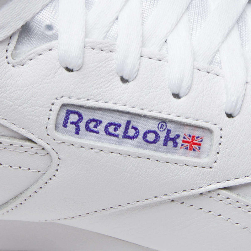 Close-up of the Men's EX-O-FIT Hi Shoes by Reebok in white leather, featuring blue stitched Reebok branding and a small Union Jack flag on a leather panel with white laces above—timeless old-school details stand out.