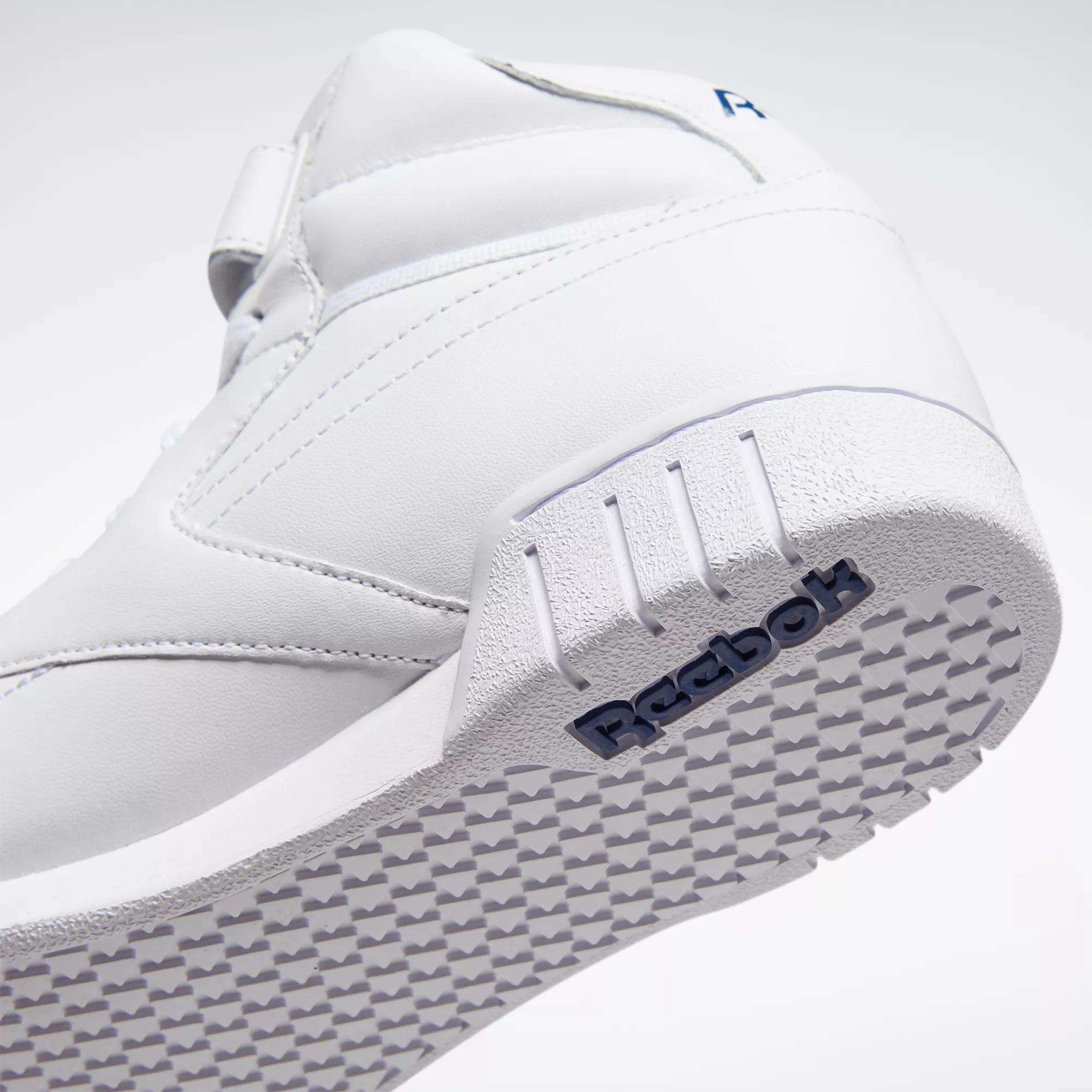 Close-up of the Men's EX-O-FIT Hi Shoes by Reebok shows the white leather upper, textured sole, and side panel with an embossed blue Reebok logo. Tilted to highlight its clean retro design and grippy outsole pattern.