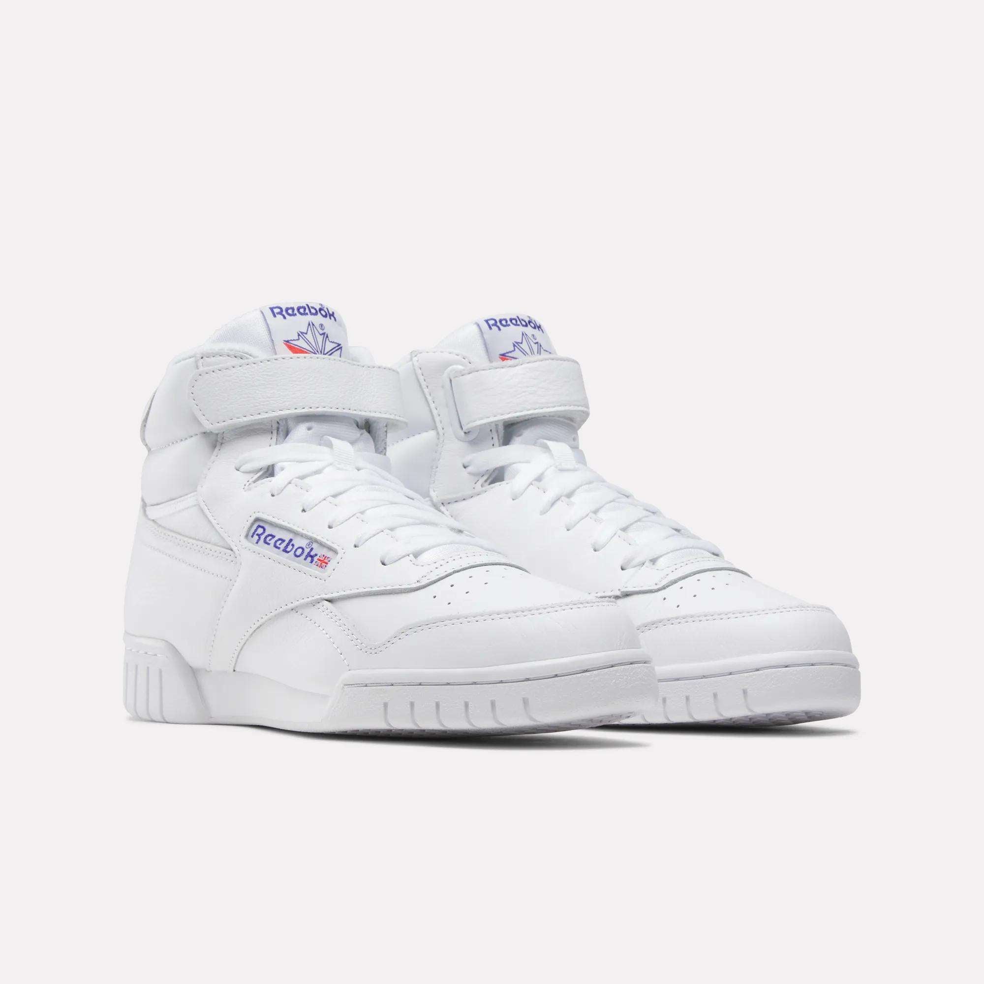 A pair of Men's EX-O-FIT Hi Shoes by Reebok, white high-top leather sneakers with velcro straps and classic blue and red logos on the side and tongue, featuring a vintage design, shown on a plain white background.