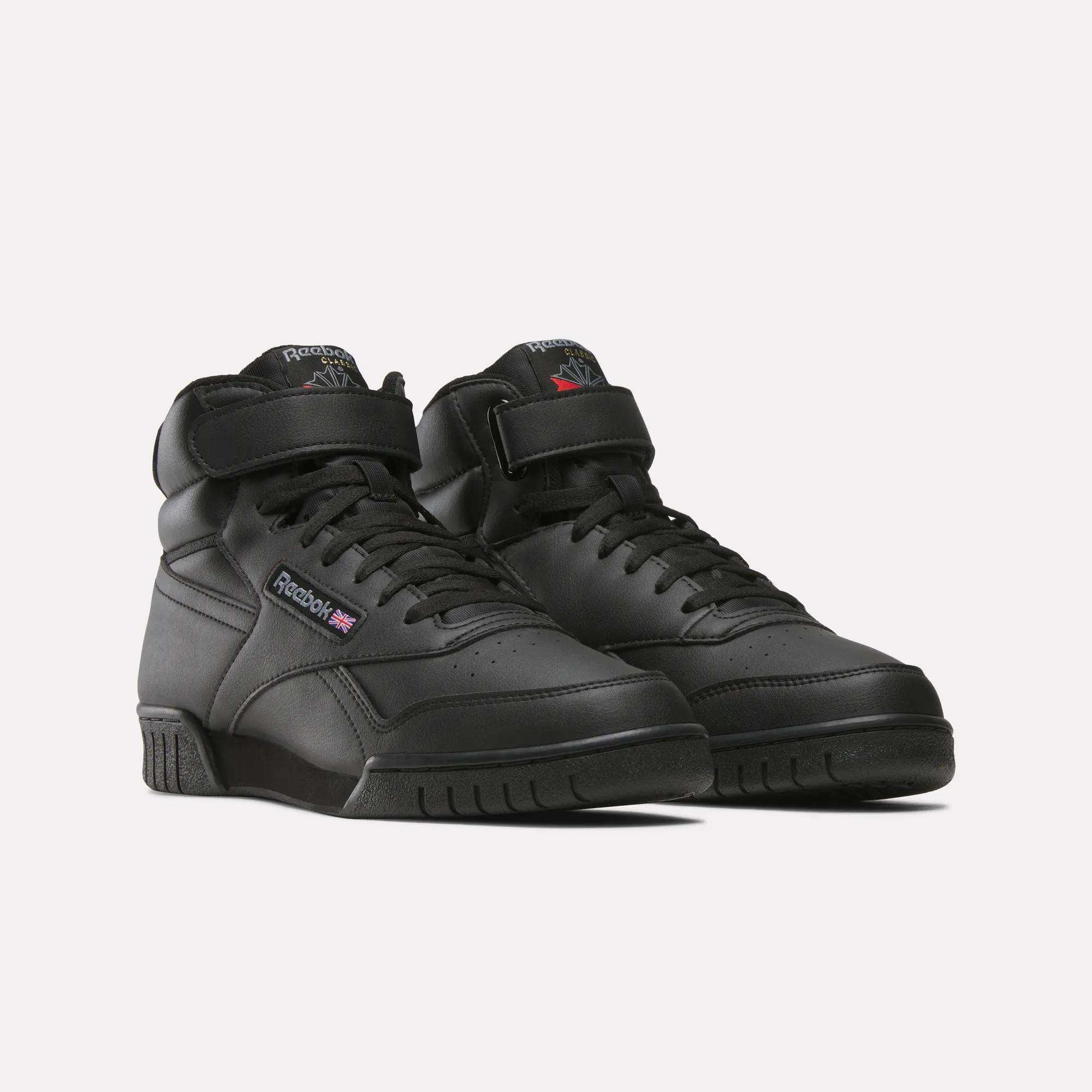 A pair of Reebok Men's EX-O-FIT Hi Shoes in black leather with a retro high-top design, Velcro straps, and the Reebok logo on the side, shown on a plain white background.