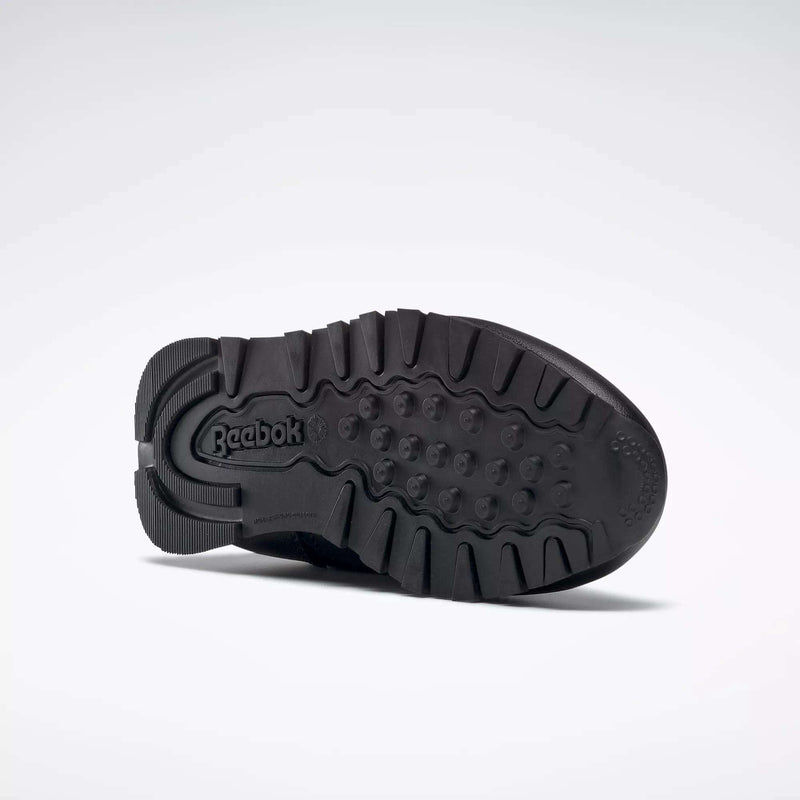 The Kids' Classic Leather Shoes - Preschool by Reebok feature a durable leather upper and a black rubber outsole with rugged treads and the Reebok logo embossed on the heel, all set against a plain light background.