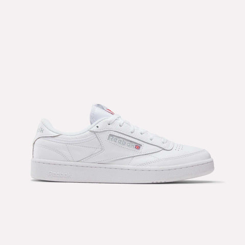 A white Reebok Club C 85 shoe with a classic low-top leather design, featuring the Reebok logo and Union Jack on the side, displayed on a plain light background. This tennis-inspired sneaker blends heritage and style.