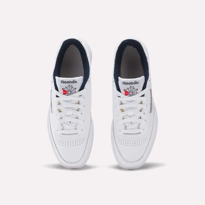 A pair of Reebok Club C 85 Shoes in white leather with navy interiors is shown from above on a plain background. These tennis-inspired sneakers have perforated toes and display the Reebok red, white, and blue logo on the tongue.