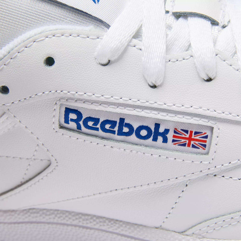 Close-up of Club C 85 Shoes by Reebok, featuring white leather, white laces, and a stitched blue Reebok logo with the British flag—classic tennis-inspired sneakers.