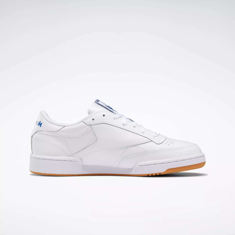 The Reebok Club C 85 Shoes are low-top white leather sneakers with a simple design, white laces, gum sole, and subtle blue branding on the heel and tongue, shown against a plain white background.