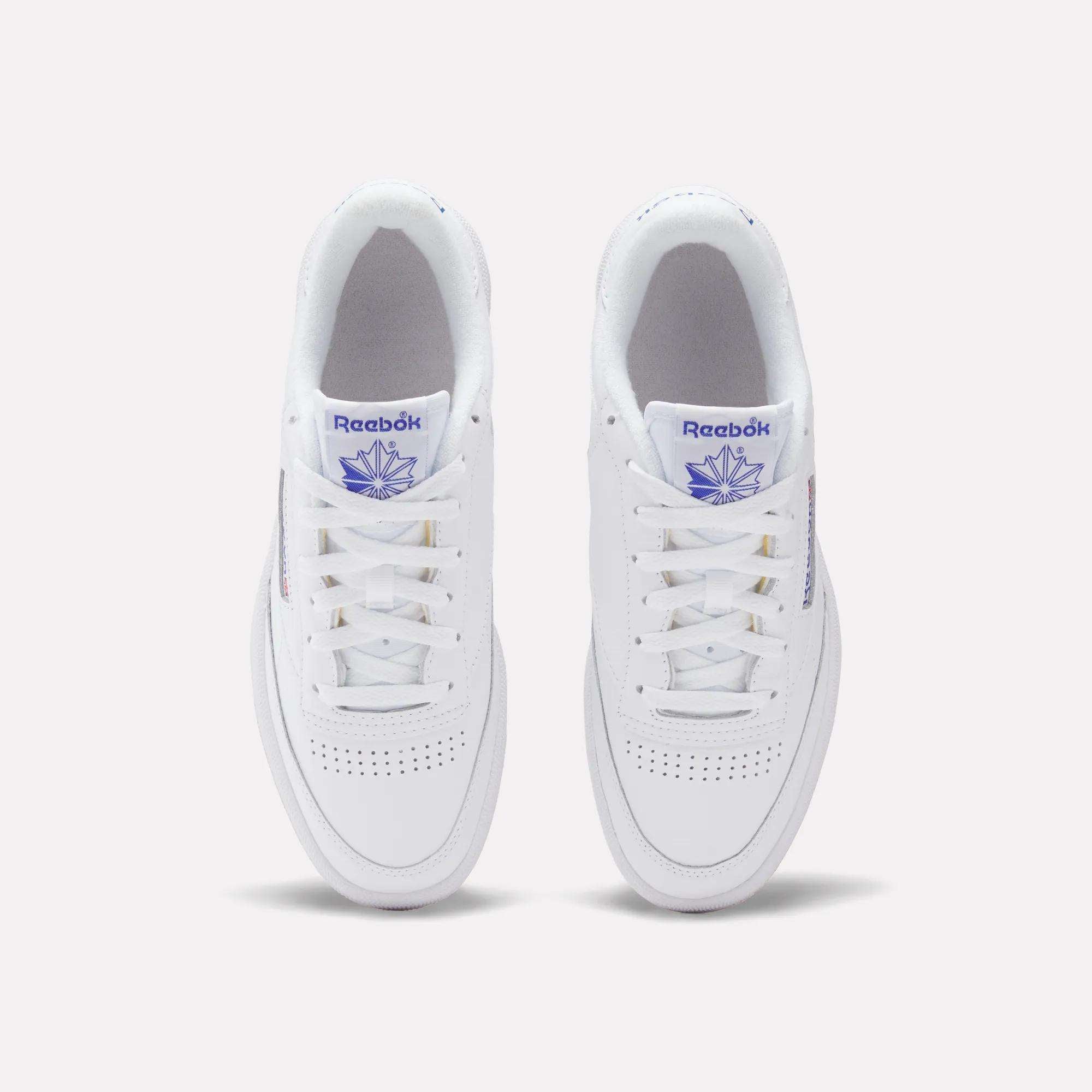 A pair of Reebok Club C 85 Shoes in white, shown from above with white laces, perforated toe boxes, and blue Reebok logos plus a stylized leaf on the tongues.