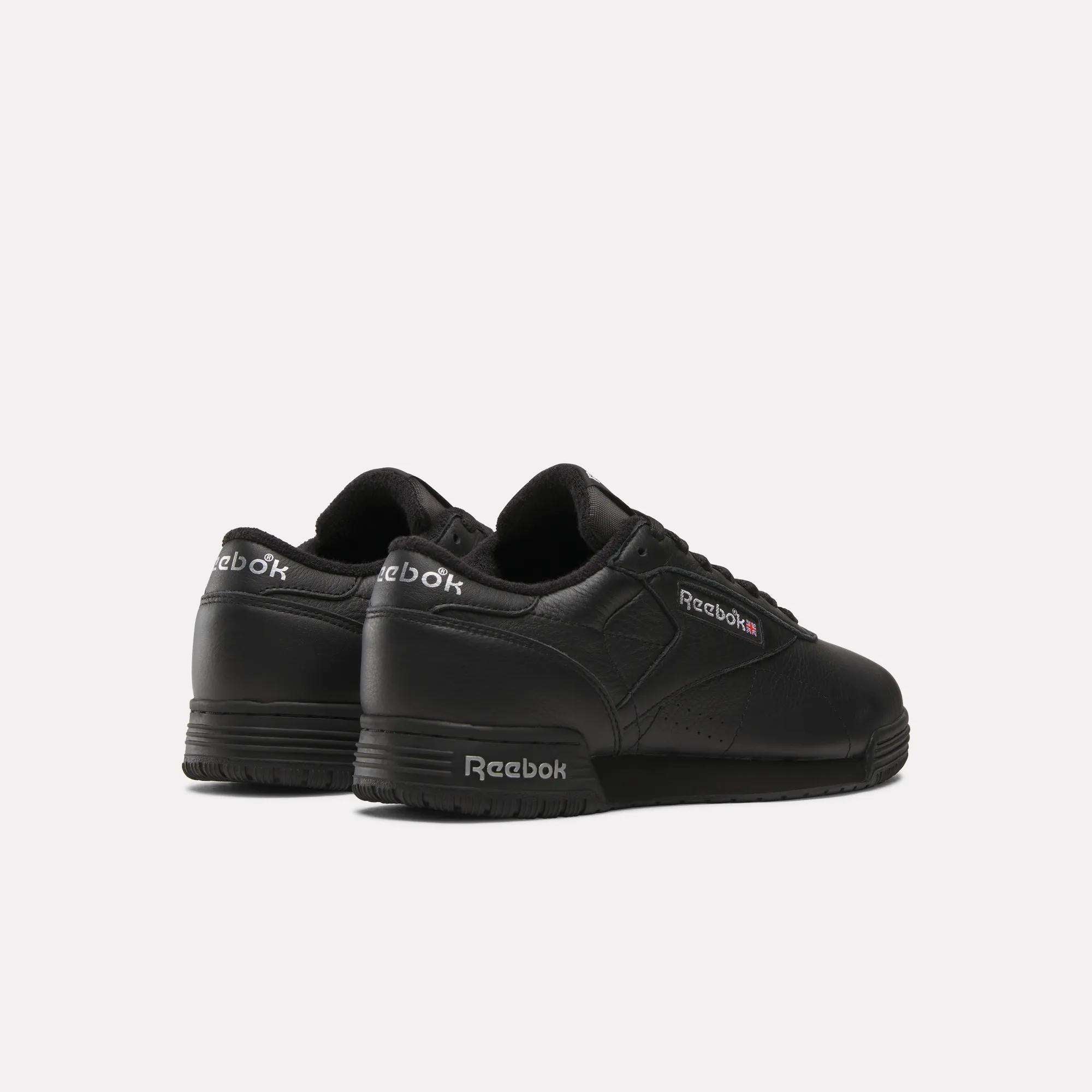 The Reebok Men's Exofit Lo Shoes are black low-top sneakers, shown from the back and side, displaying the Reebok logo in white and red on the side and heel against a plain white background.