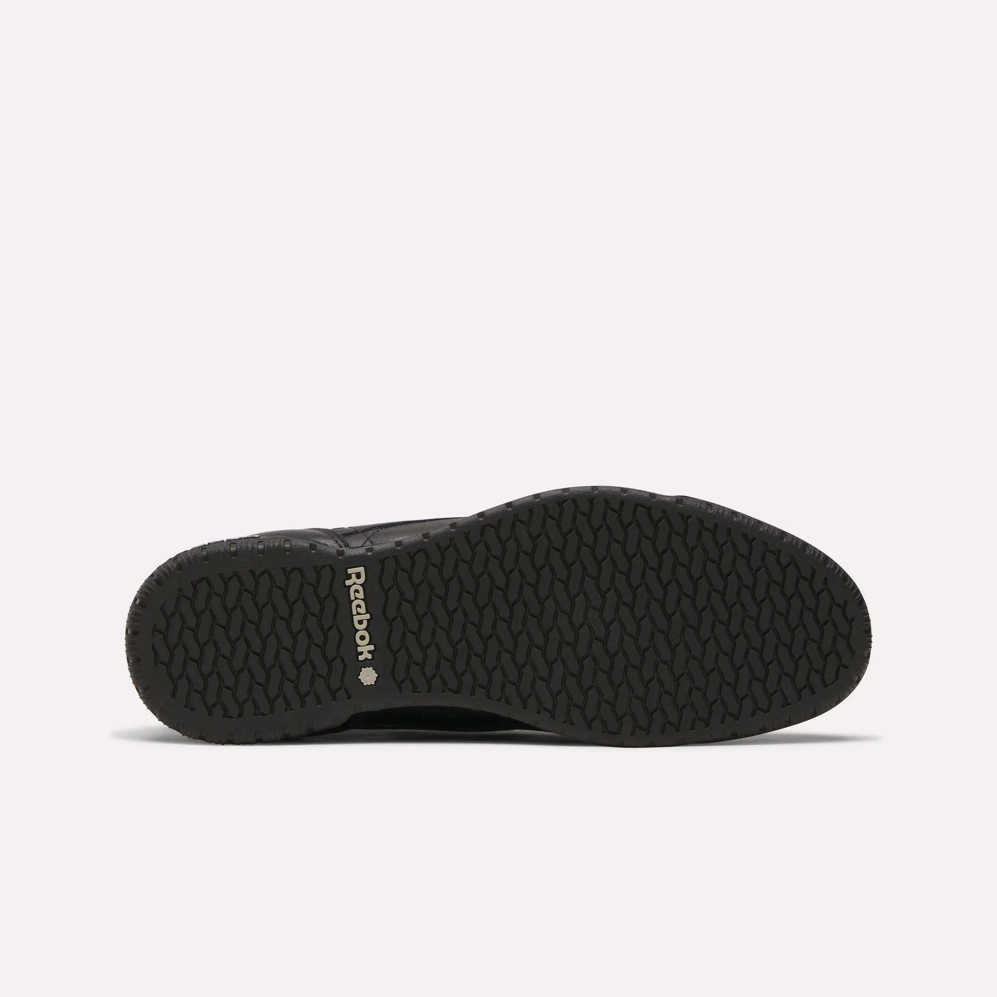 Men’s Exofit Lo Shoes by Reebok shown from the bottom, displaying a black low-profile design with a textured rubber sole and light Reebok branding near the heel on a plain, light background.