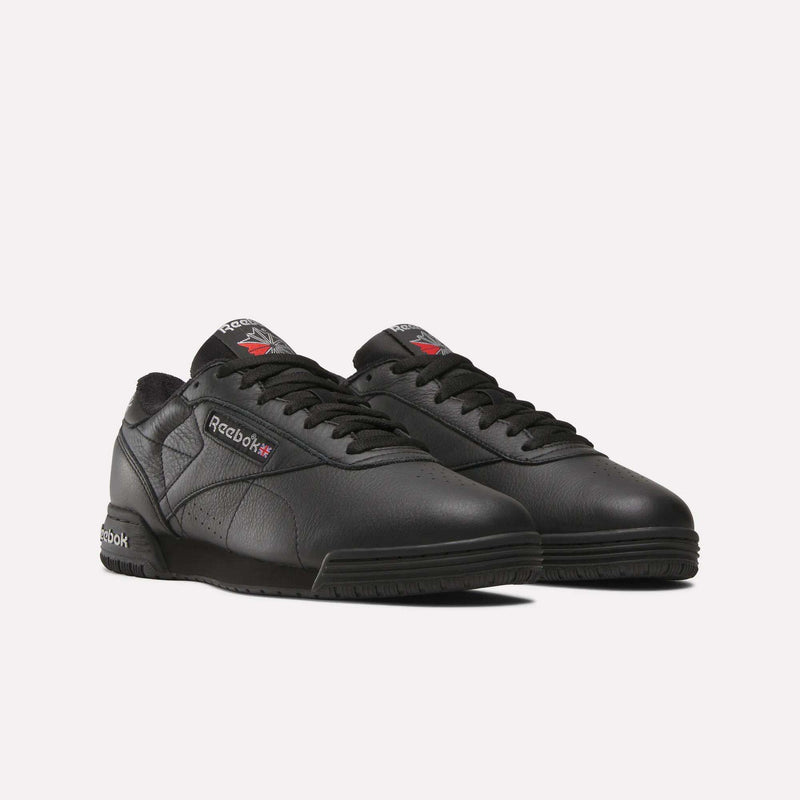 A pair of Reebok Men's Exofit Lo Shoes in black, featuring a low-top lace-up design and subtle red and white Reebok logos on the side, tongue, and heel, displayed against a plain white background.