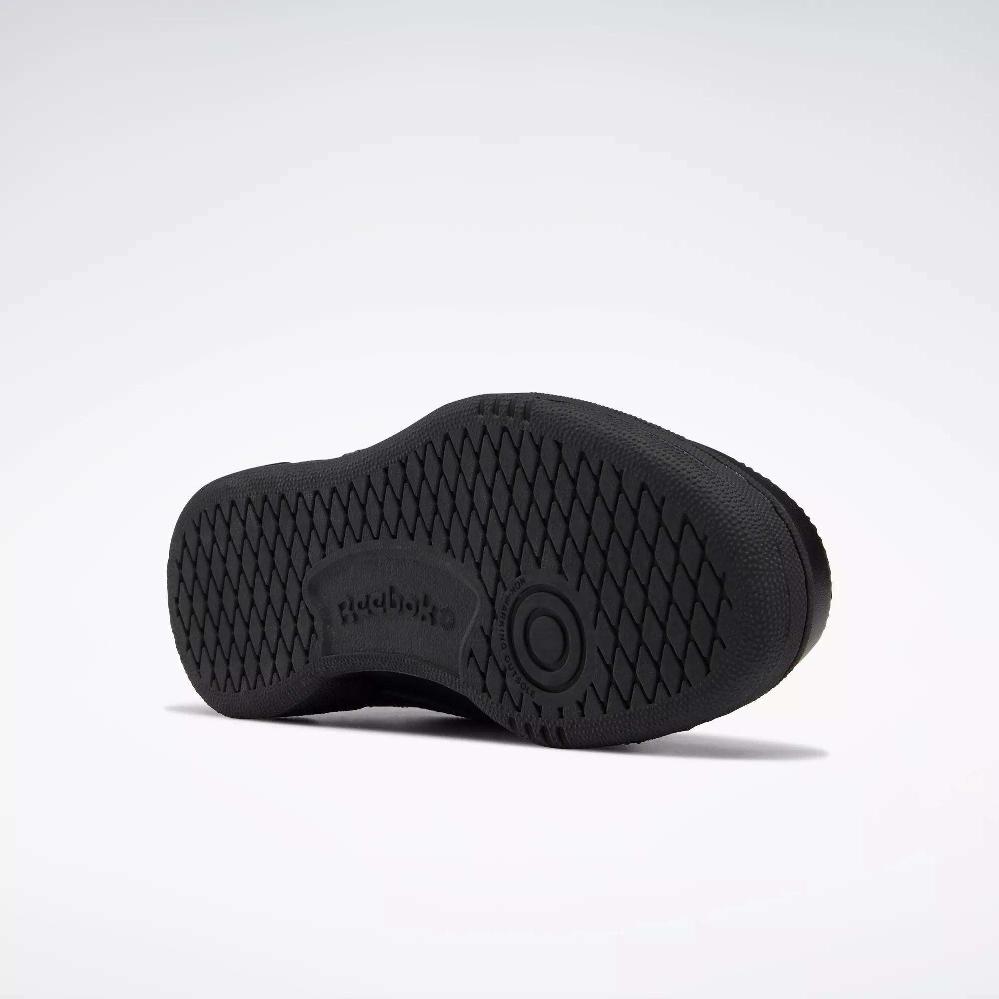 The image shows the sole of a black Reebok Kids' Club C Shoe - Grade School, with a high-abrasion rubber outsole, diamond-patterned grip, Reebok logo, and a circular design at the center. The background is plain white.