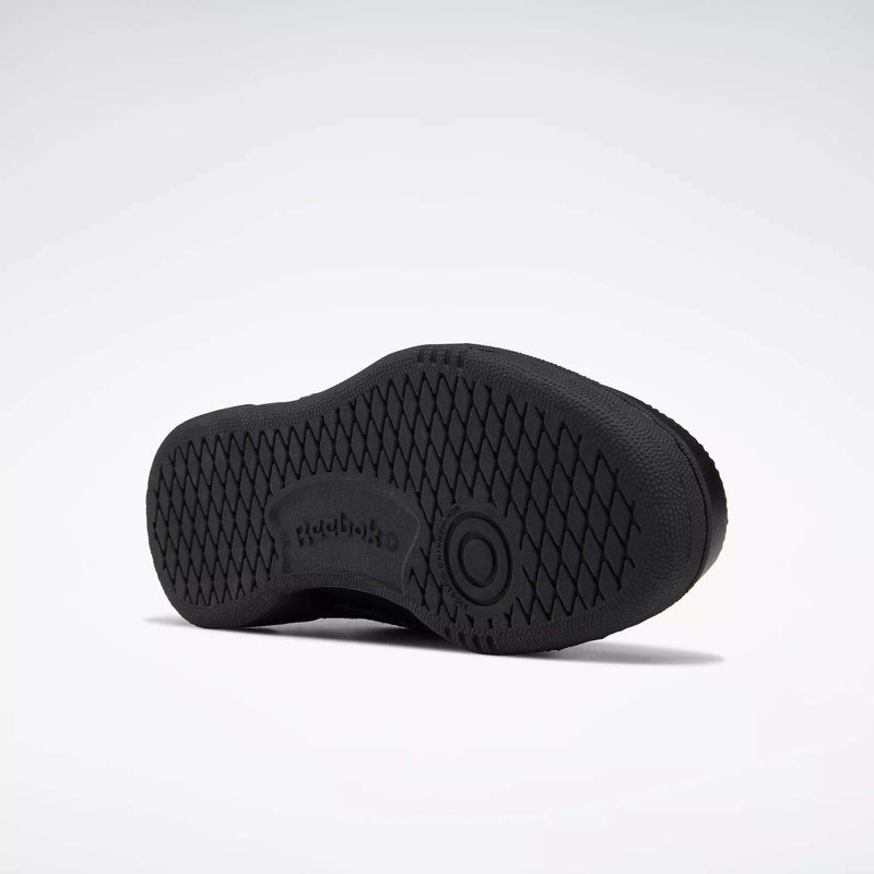 The image shows the sole of a black Reebok Kids' Club C Shoe - Grade School, with a high-abrasion rubber outsole, diamond-patterned grip, Reebok logo, and a circular design at the center. The background is plain white.