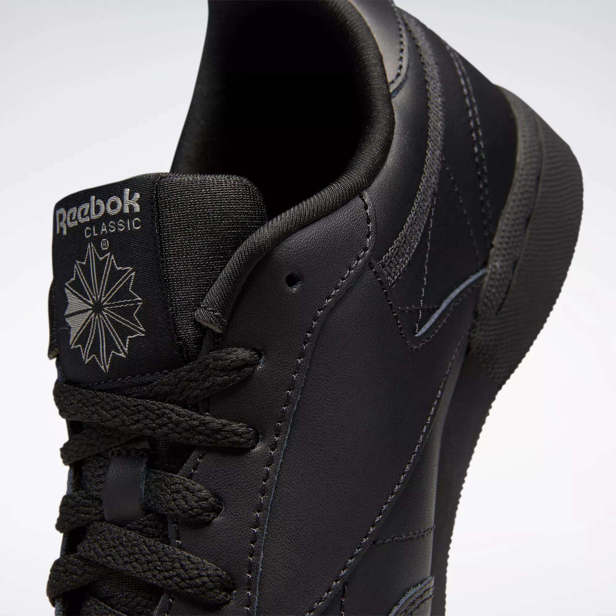 Close-up of black Reebok Kids' Club C Shoes (Grade School), featuring smooth leather uppers, the tongue with Reebok logo and starburst design, black laces, and detailed stitching.