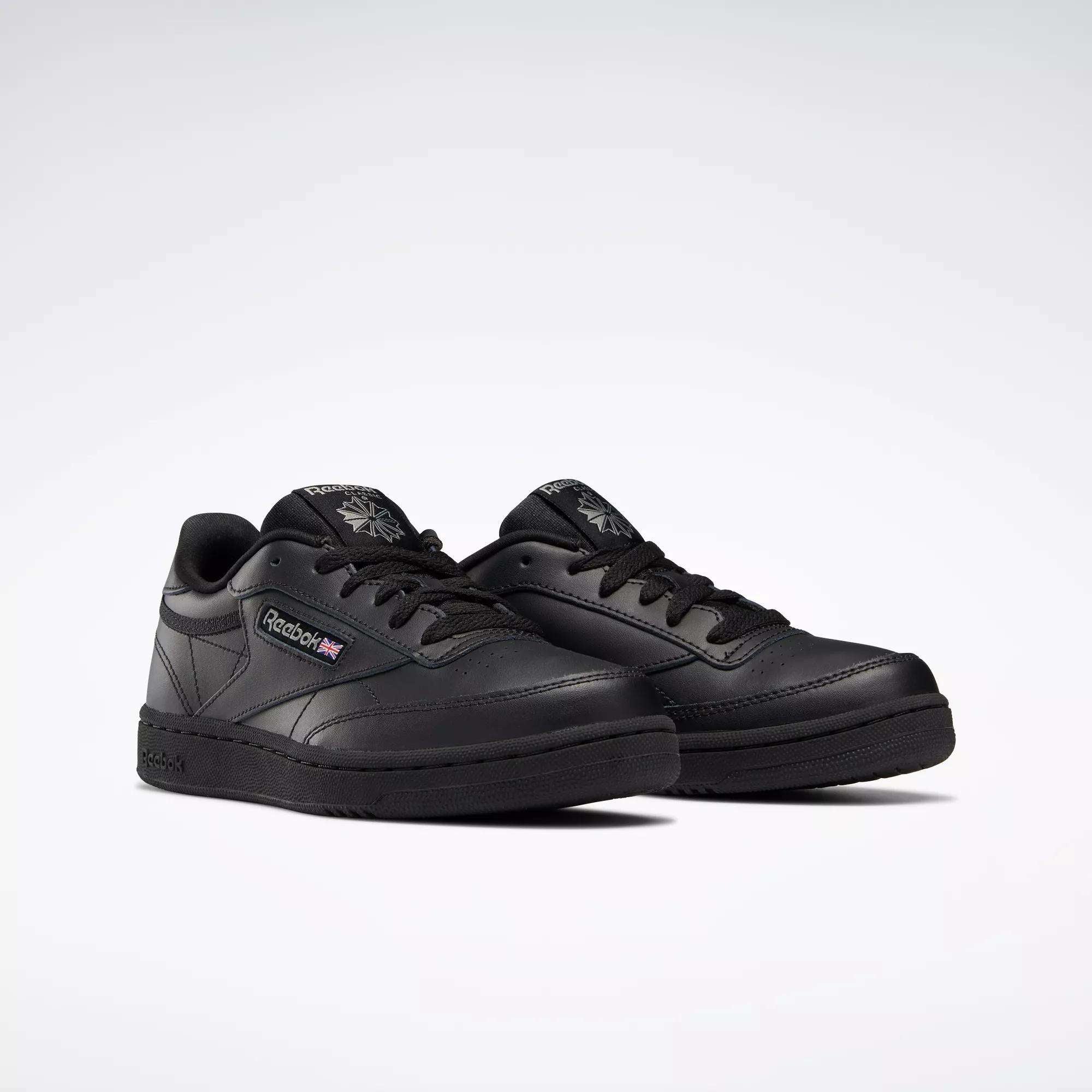 A pair of Reebok Kids' Club C Shoes - Grade School with black leather uppers, black soles and laces, the Reebok logo and a small Union Jack on the side, displayed on a plain white background.