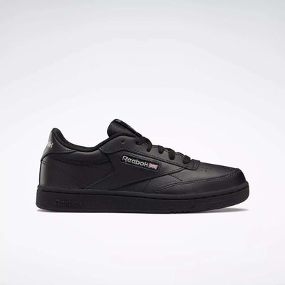 The Kids' Club C Shoes – Grade School by Reebok are black low-tops with soft leather uppers, black laces, a black sole with high-abrasion rubber outsole, plus the Reebok logo and Union Jack on the side, shown on a light background.