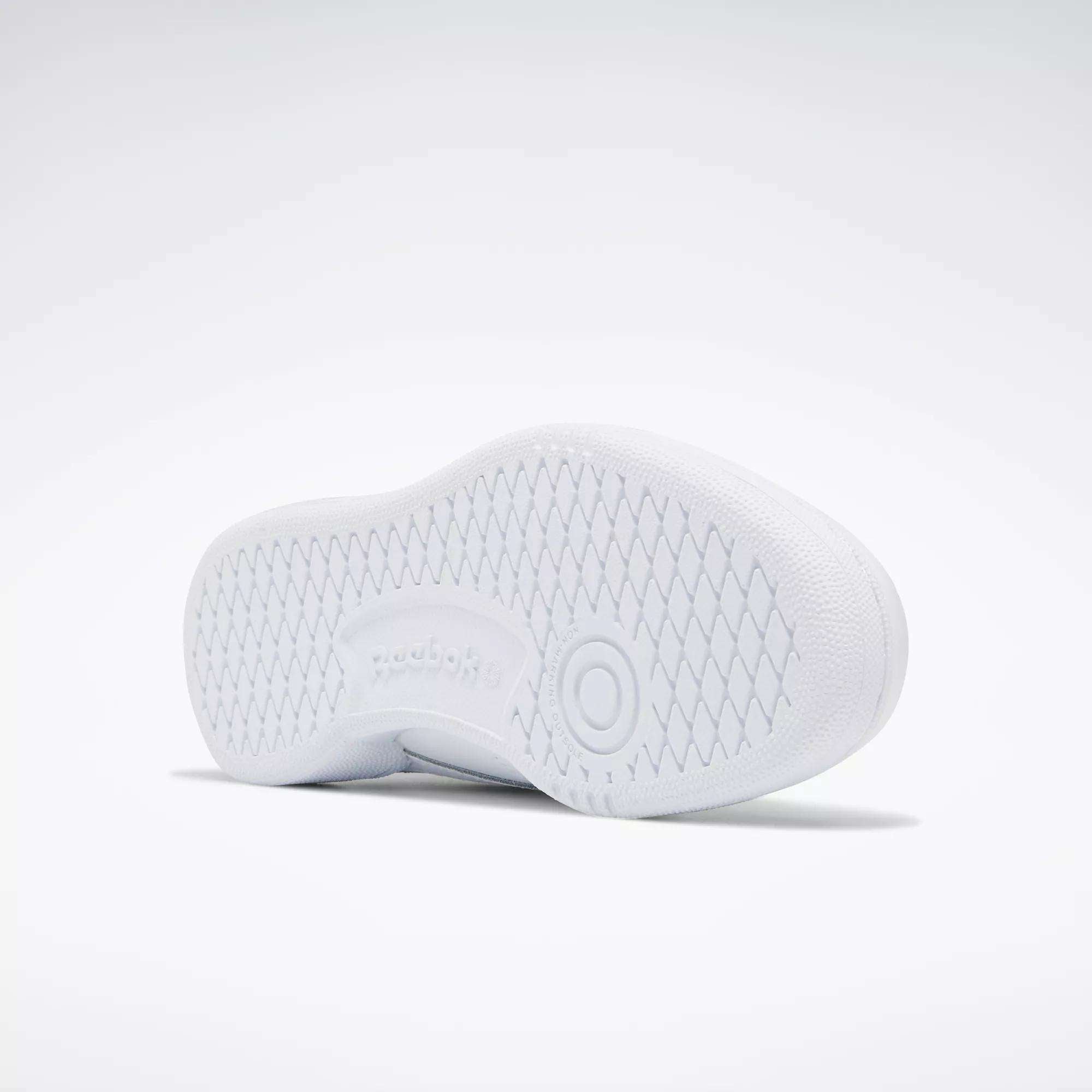 The image shows the white sole of the Kids' Club C Shoes - Grade School by Reebok, featuring a textured diamond pattern, a circular design near the heel, and an embossed Reebok logo in the center of the high-abrasion rubber outsole.