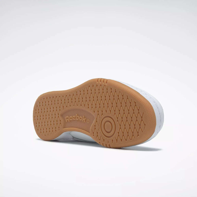 The image shows the underside of a white Reebok Kids' Club C Shoe - Grade School, featuring a high-abrasion rubber outsole with the Reebok logo and a circular pattern near the ball of the foot, classic to court shoes.