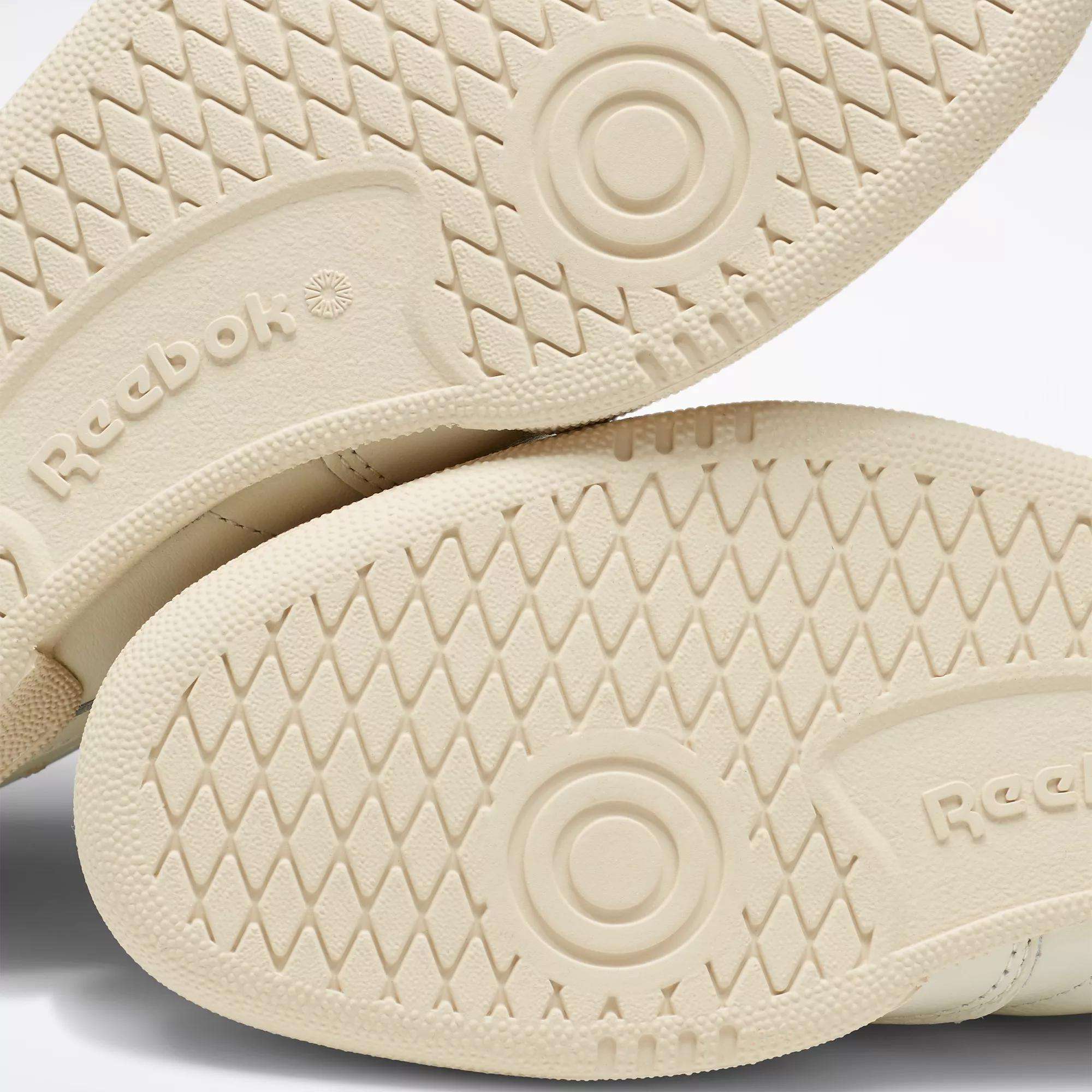 Close-up of the beige rubber soles of Reebok Club C 85 Vintage Shoes, showing a diamond-patterned tread, circular grip details, and the embossed Reebok logo.