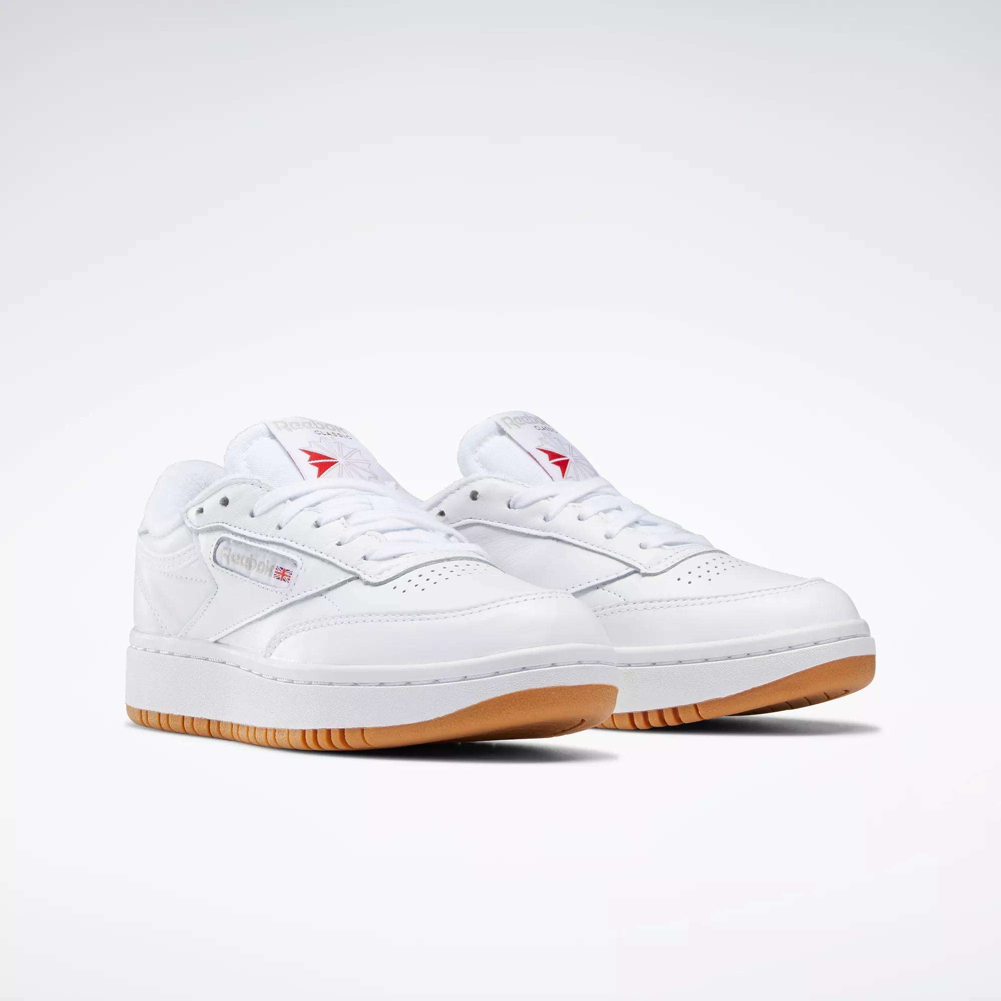 The Reebok Women's Club C Double Shoes are shown on a light gray background, featuring white leather, gum soles, subtle stitching, classic branding, and a low-cut tennis-inspired design.