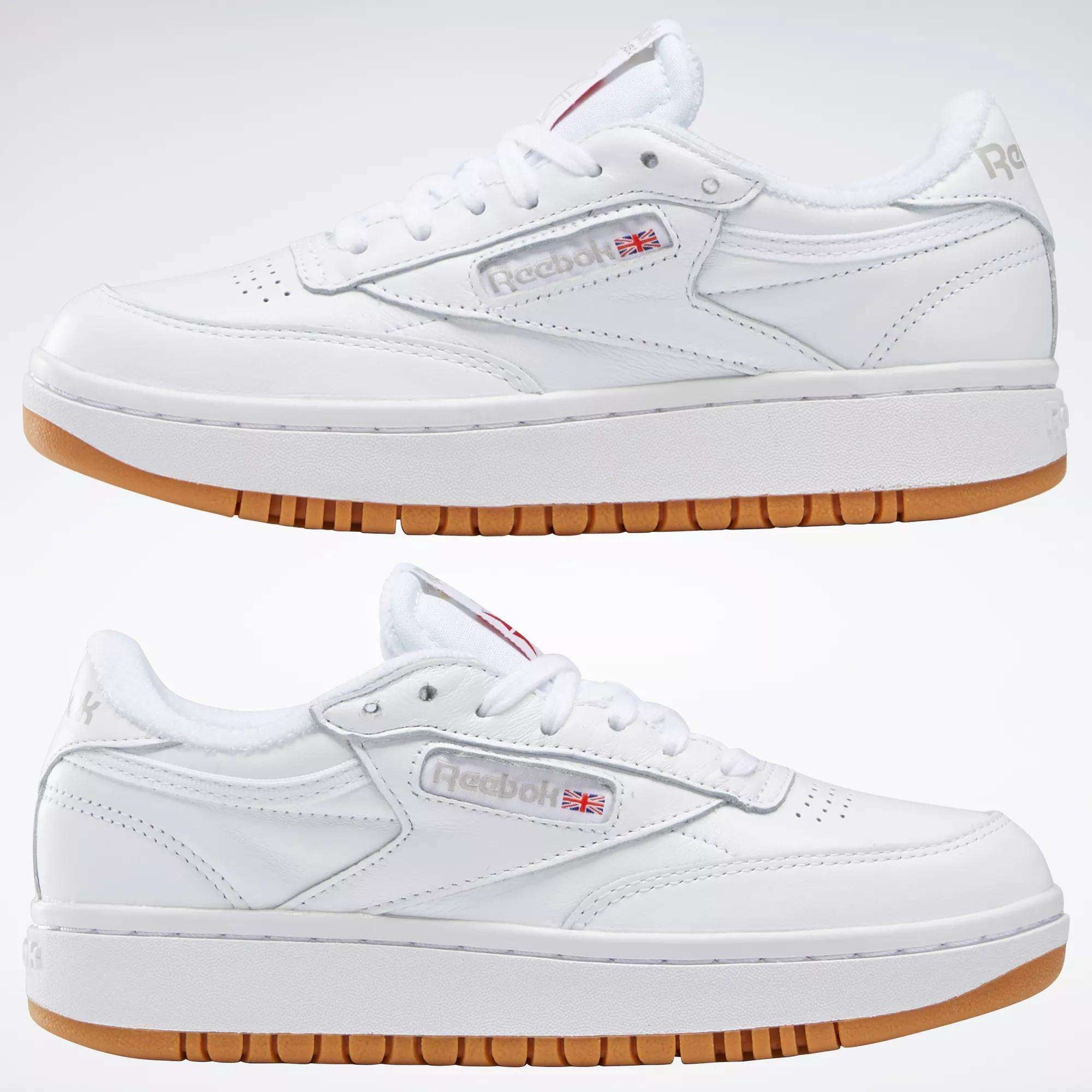 Two white Reebok Women's Club C Double Shoes with gum soles are shown side by side on a plain white background, featuring leather uppers, a stylish platform midsole, the Reebok logo, and a small Union Jack flag on the side.