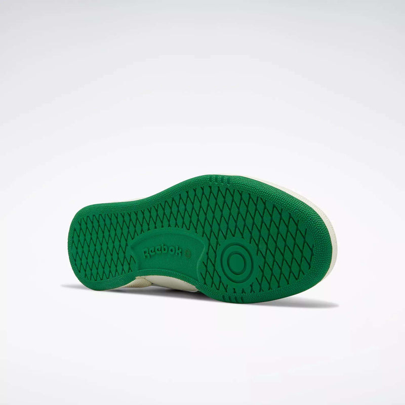 The image features the sole of a Men's Club C Revenge Vintage Shoe by Reebok, displayed on its side. The green, textured pattern and circular detailing create a retro look, with the Reebok logo visible against the white background.