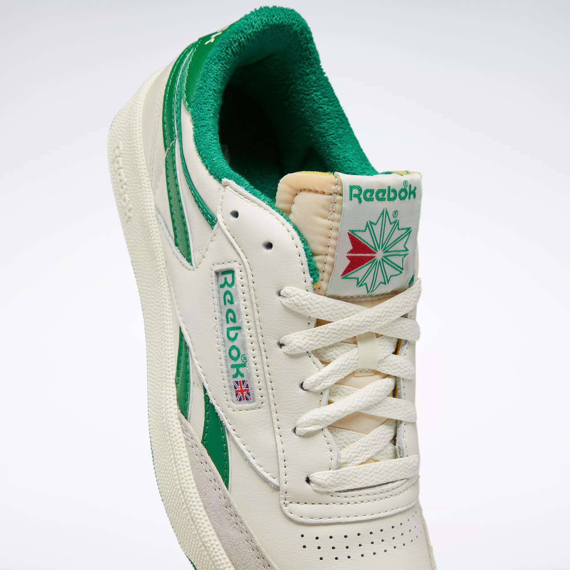 The Reebok Men's Club C Revenge Vintage Shoes feature white vintage-style leather, green accents, a red and green star on the tongue, the Reebok logo, and a small Union Jack flag on the side for retro flair.