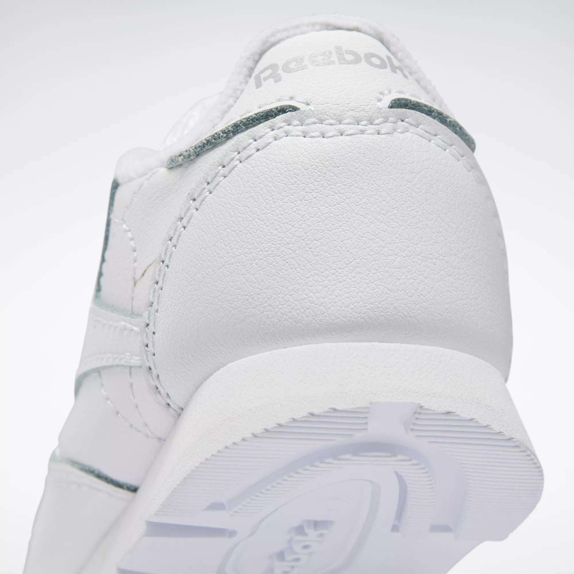 Close-up of the heel on Reebok Kids' Classic Leather Shoes – Baby & Toddler, featuring textured stitching, part of the outsole, and an embossed Reebok logo—ideal for little ones’ daily adventures.