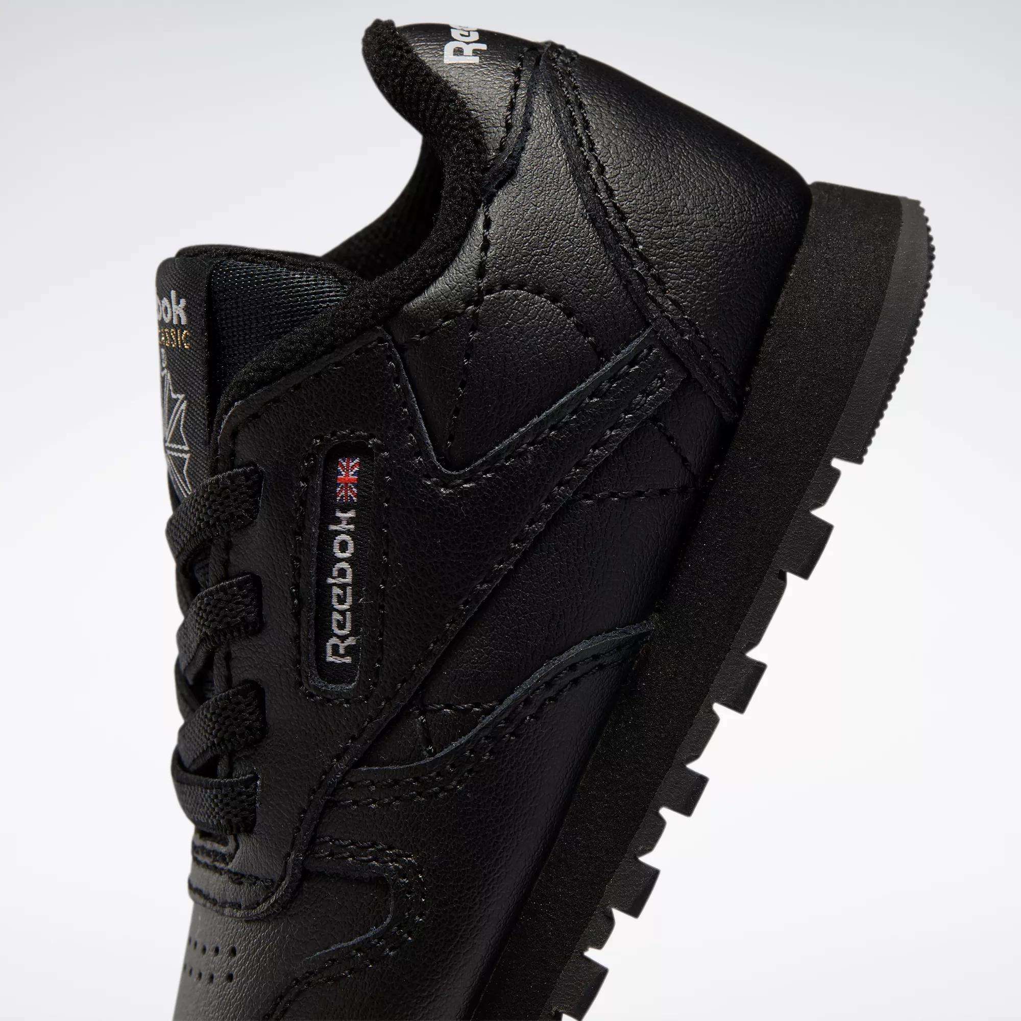 Close-up of Kids' Classic Leather Shoes by Reebok for babies and toddlers, featuring a black design with visible logo, black laces, and rugged sole, showcasing retro sneaker style against a plain white background.