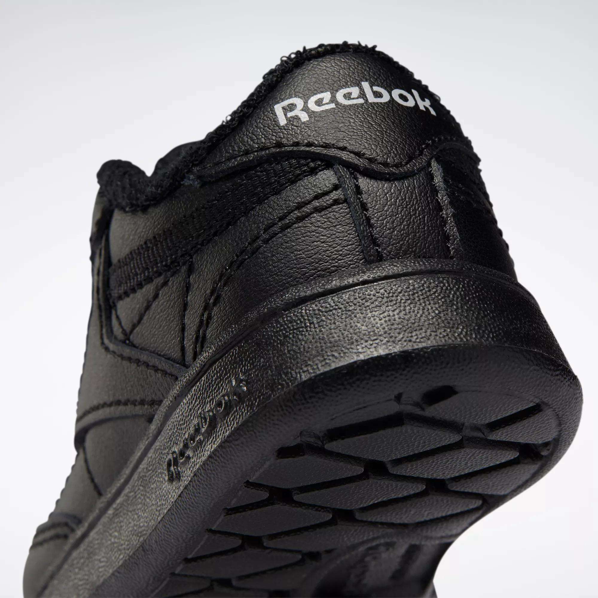 Close-up of the heel and sole of a black Reebok Kids' Club C Shoe for babies and toddlers, featuring soft leather, the Reebok logo on the heel, and textured sole patterns. The shoe is tilted upward against a plain light background.