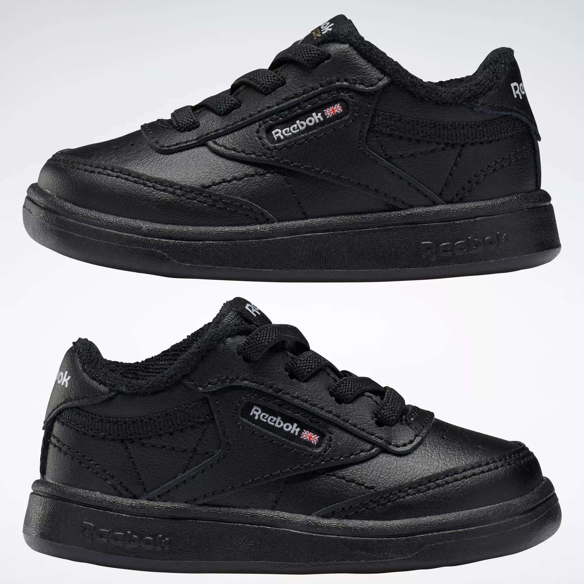 Two black Reebok Kids' Club C Shoes for babies and toddlers are displayed side by side on a white background, featuring soft leather uppers, textured soles, and visible logo details.
