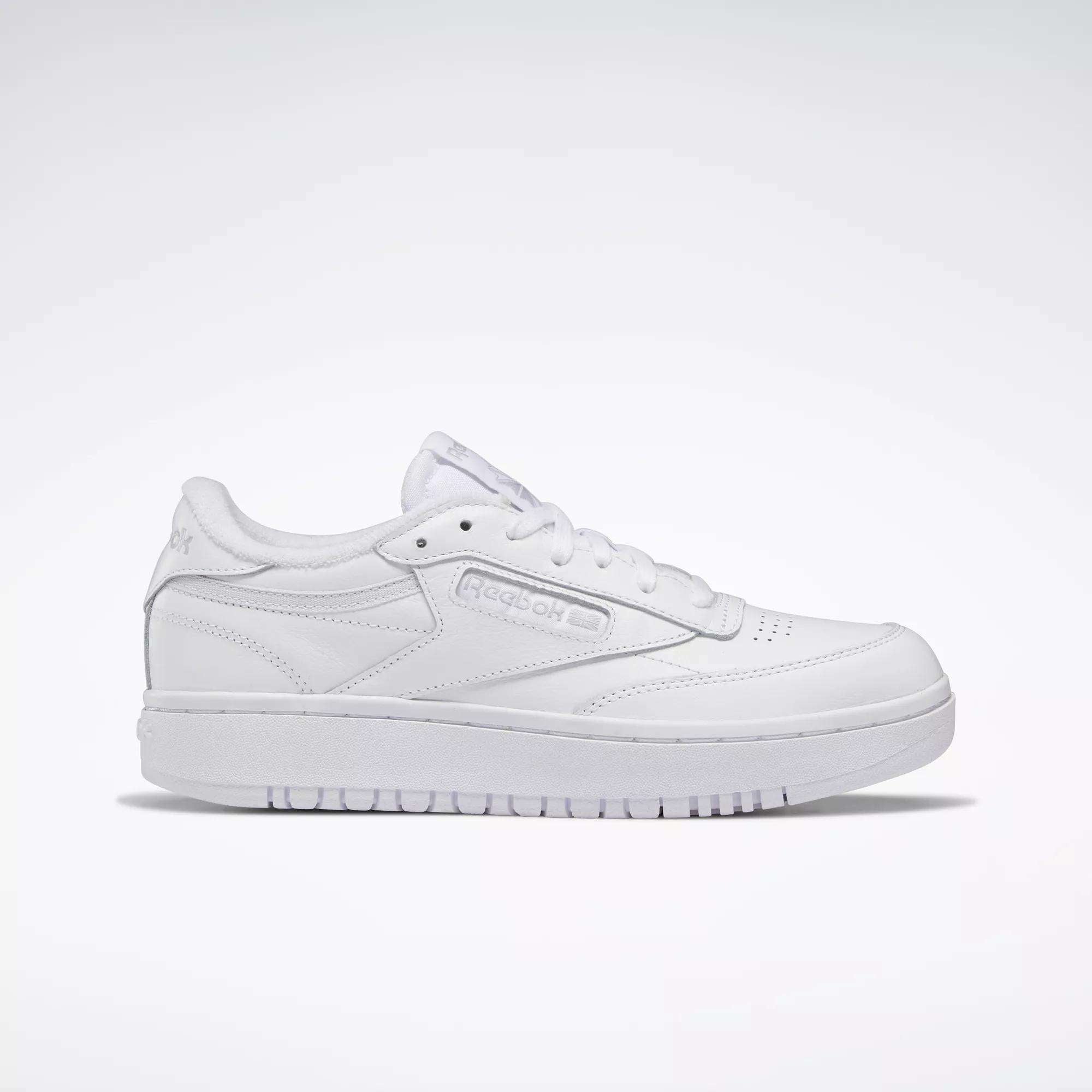 A side view of the Women's Club C Double Shoes by Reebok, featuring a classic white low-top design, lace-up front, subtle side branding, and tennis-inspired style against a plain light background.