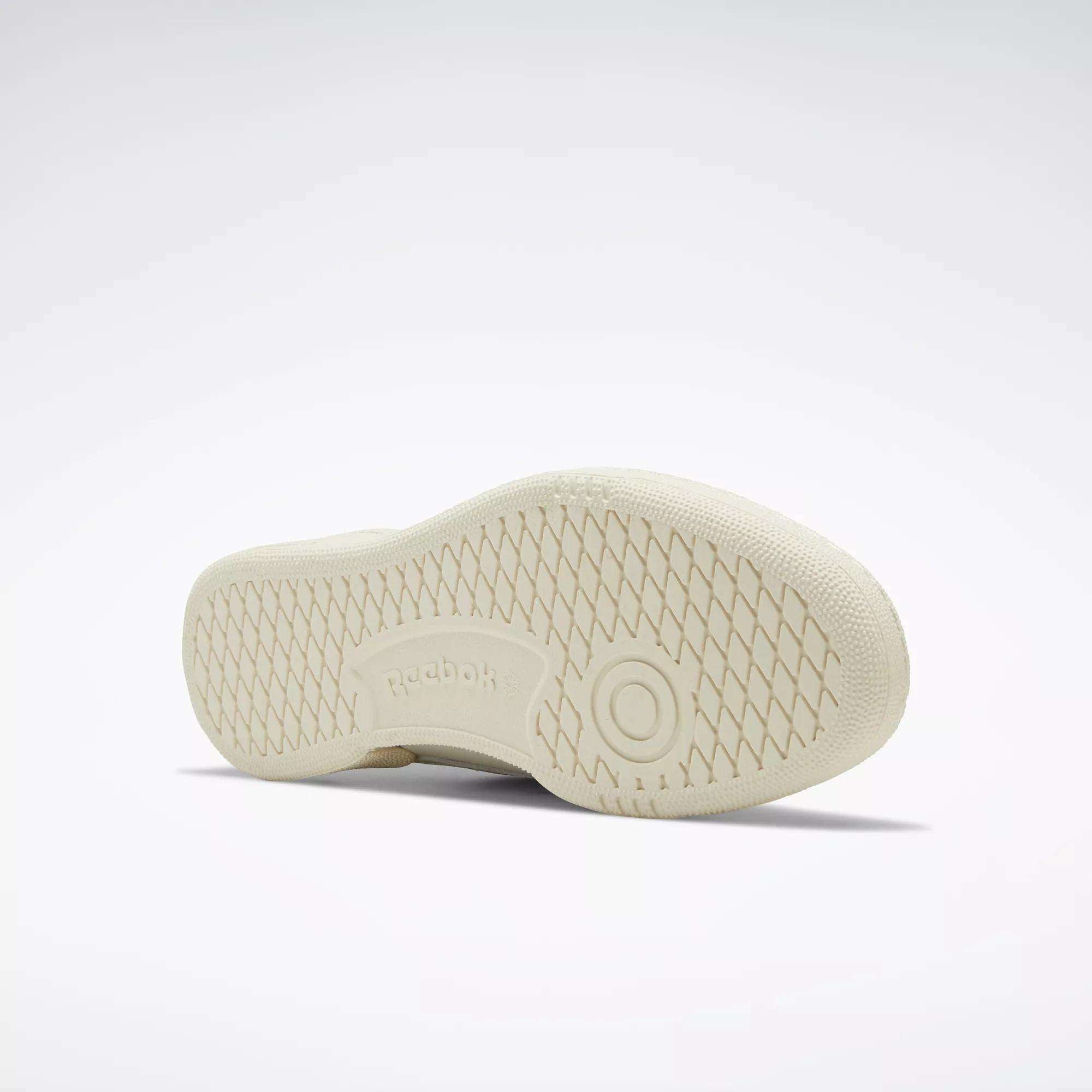 The image displays the sole of a beige Reebok Club C 85 Vintage Shoe, featuring a textured crisscross pattern, embossed Reebok logo at the center, and circular heel detail. The background is plain and light-colored.
