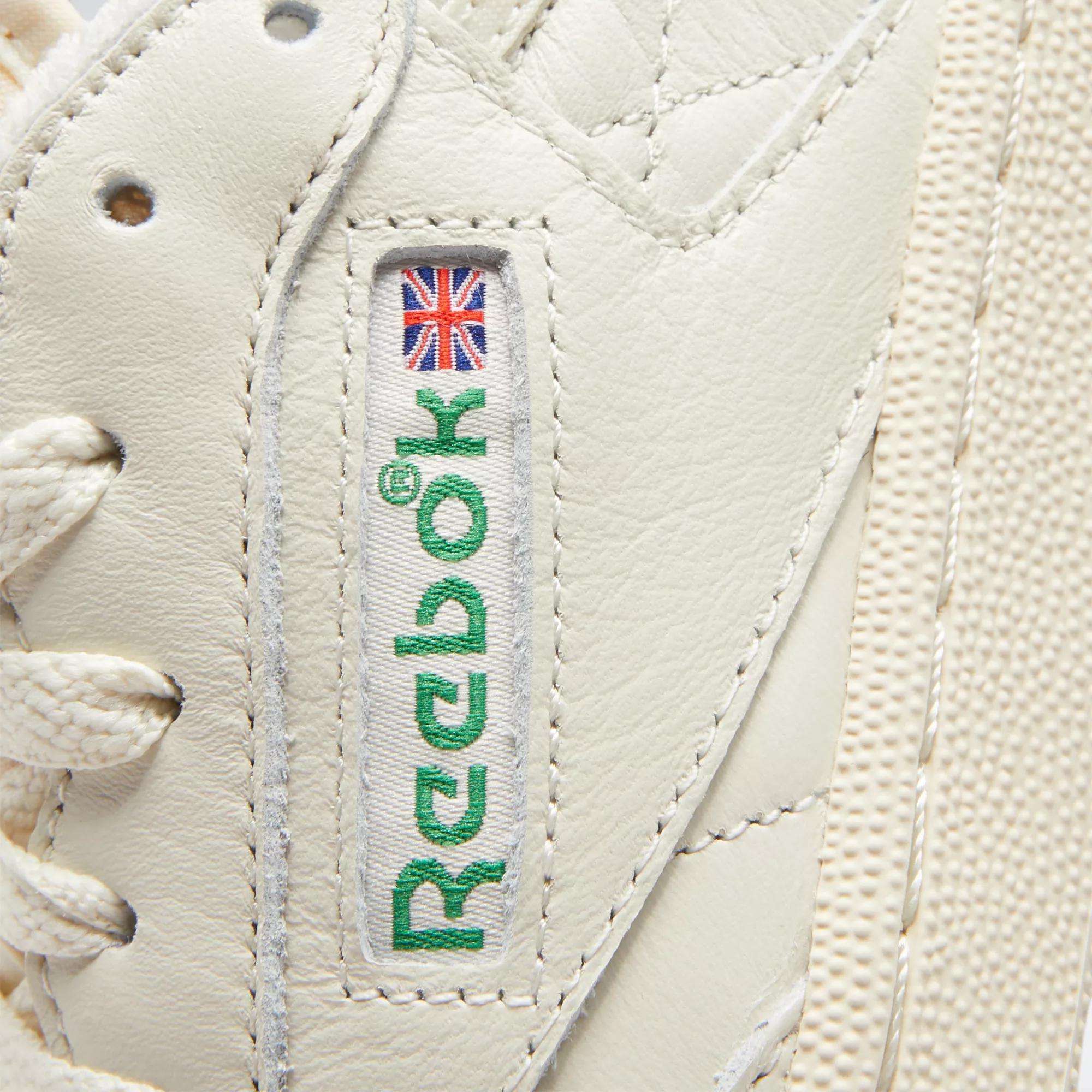 Close-up of Reebok Women's Club C 85 Vintage Shoes in white, showcasing the stitched green Reebok logo with a small Union Jack, white laces, and premium textured leather.
