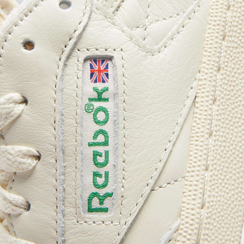 Close-up of Reebok Women's Club C 85 Vintage Shoes in white, showcasing the stitched green Reebok logo with a small Union Jack, white laces, and premium textured leather.
