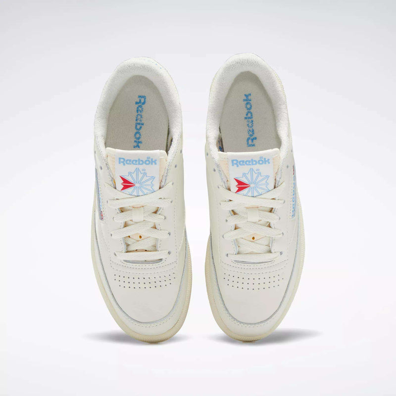 A pair of Reebok Women's Club C 85 Vintage Shoes in off-white, seen from above, with blue Reebok logos on the tongues and insoles, white laces, and subtle perforations on the toe boxes.