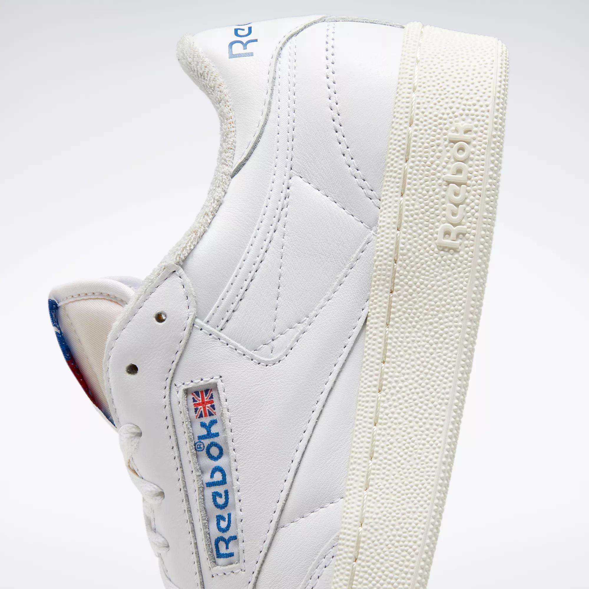 A close-up of Reebok Club C 85 Vintage Shoes shows their white leather upper, textured cream sole with lightweight cushioning, blue and red Reebok logo, and Union Jack flag on the side, angled to reveal both the side and part of the sole.