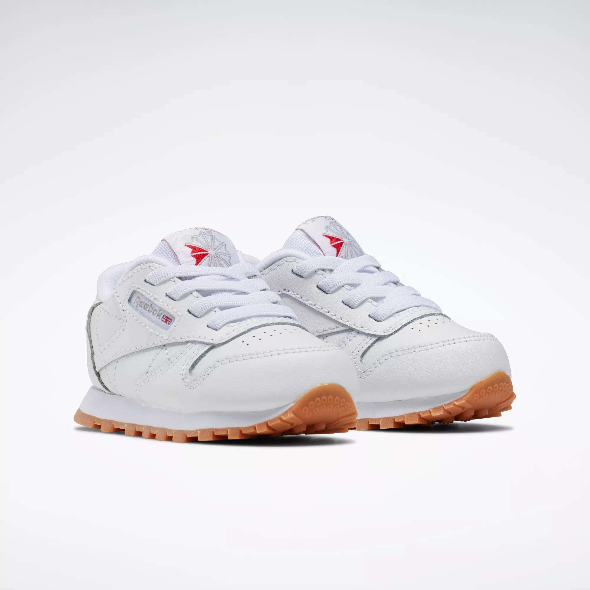 The Reebok Kids' Classic Leather Shoes for toddlers feature a clean white design with gum rubber soles and red and grey Reebok logos on the tongue and side.