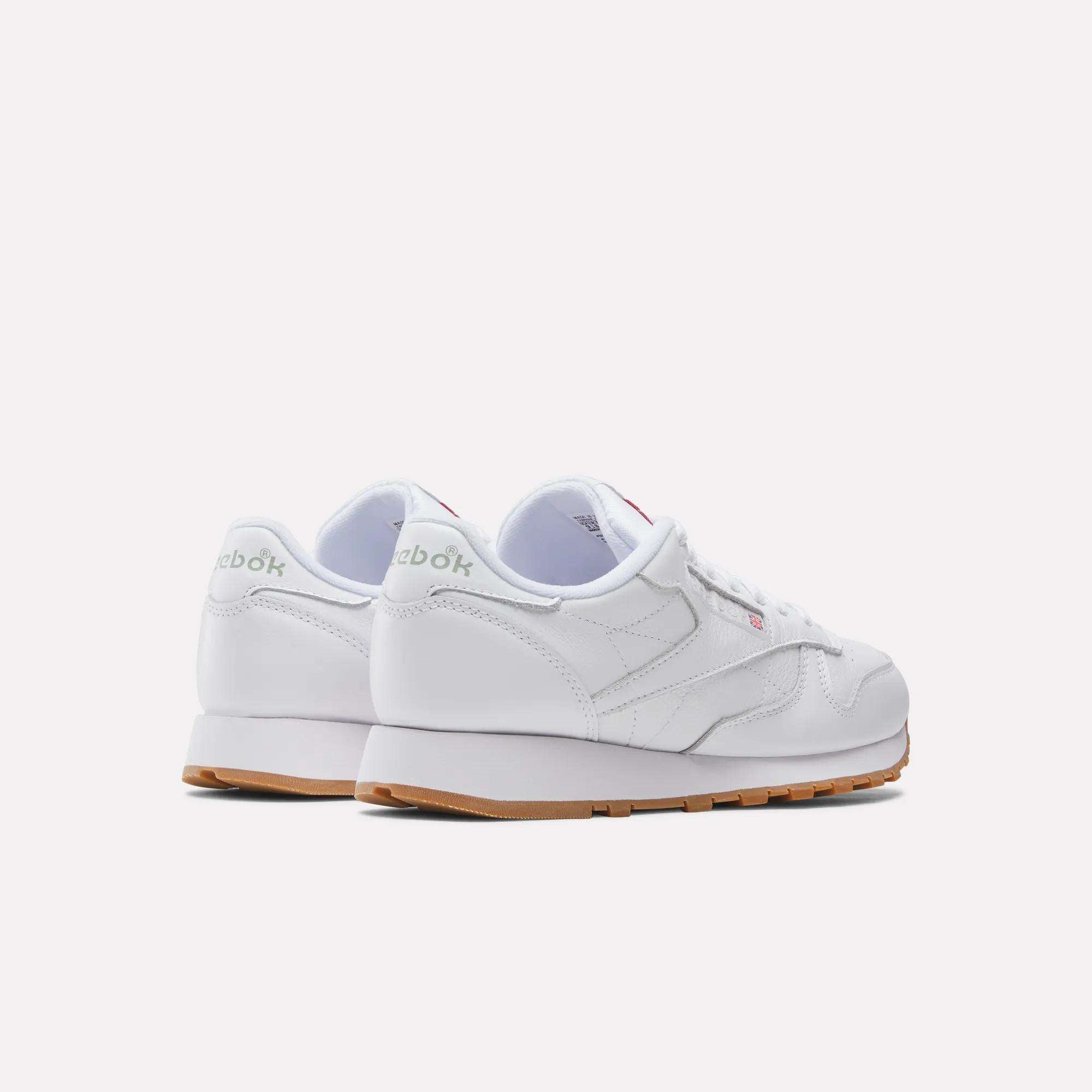 A pair of white Reebok Classic Leather Shoes with gum soles is shown from the back and side on a plain white background. These retro shoes have a durable leather upper, with the Reebok logo visible on the heel and side.