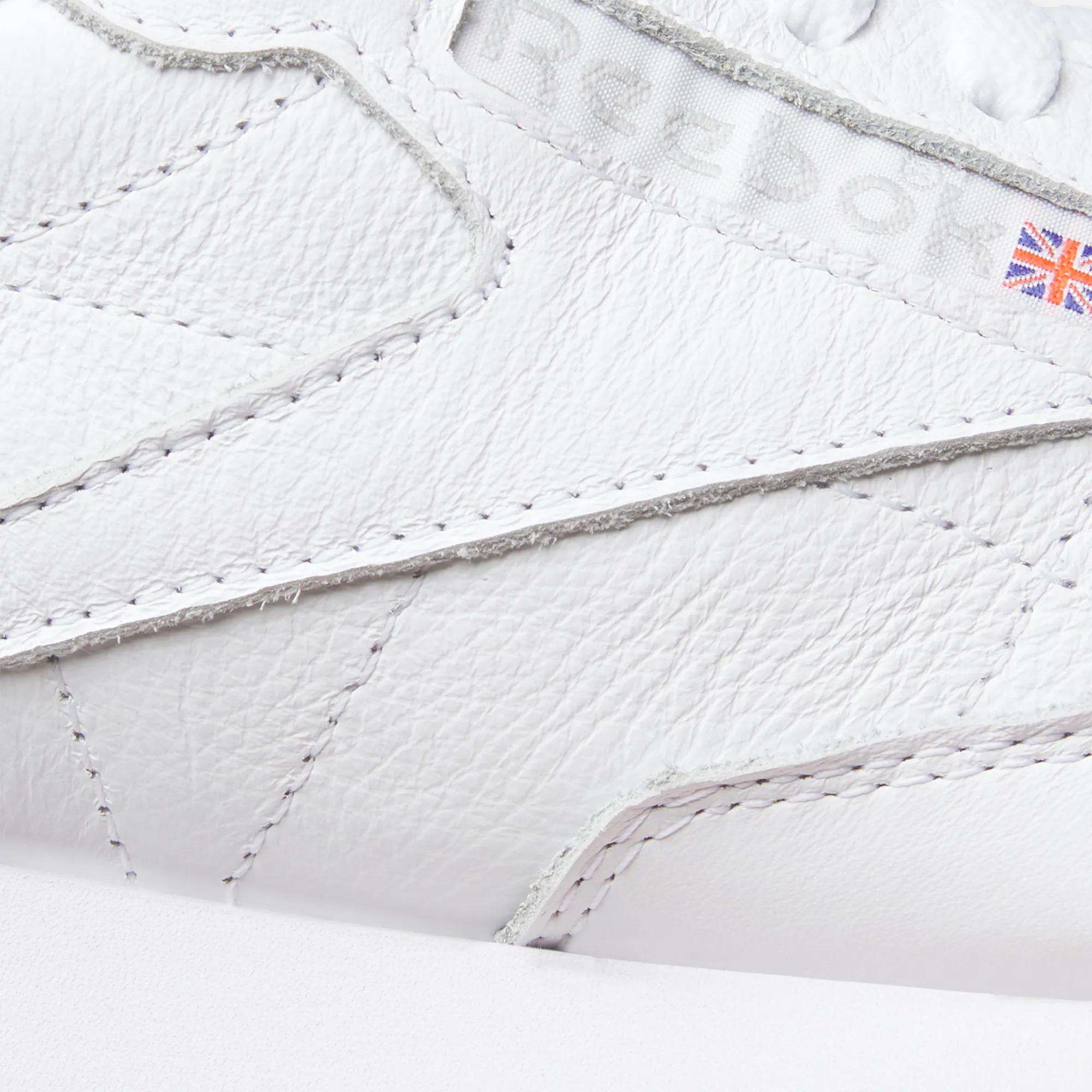 Close-up of Reebok Classic Leather Shoes features detailed stitching, an embossed logo, leather upper, and a Union Jack flag patch for authentic retro style.