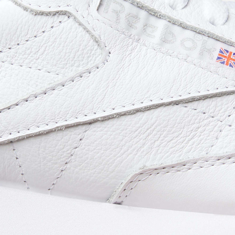 Close-up of Reebok Classic Leather Shoes features detailed stitching, an embossed logo, leather upper, and a Union Jack flag patch for authentic retro style.